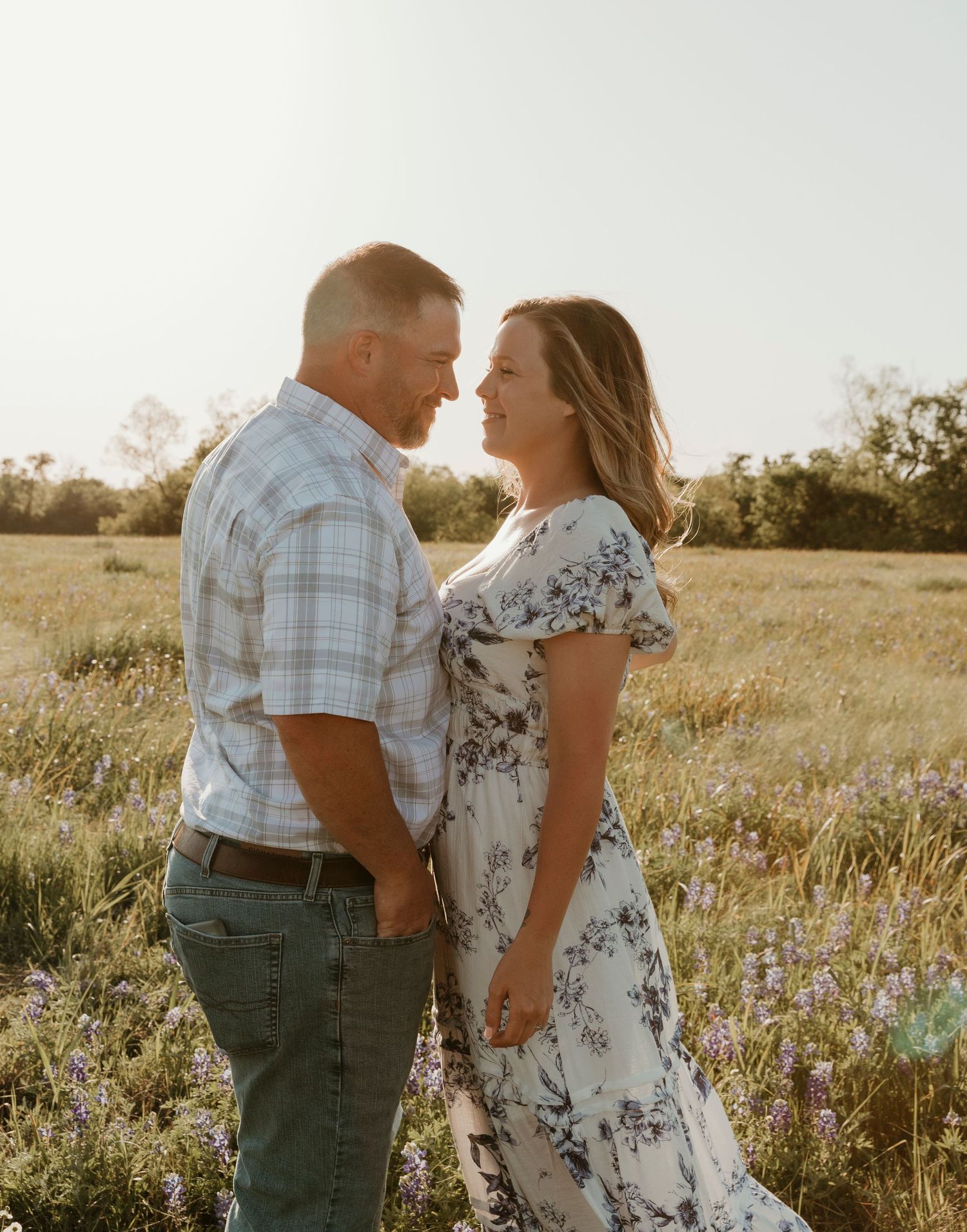 Couple sharing an intimate moment in a sun-lit field with wildflowers.