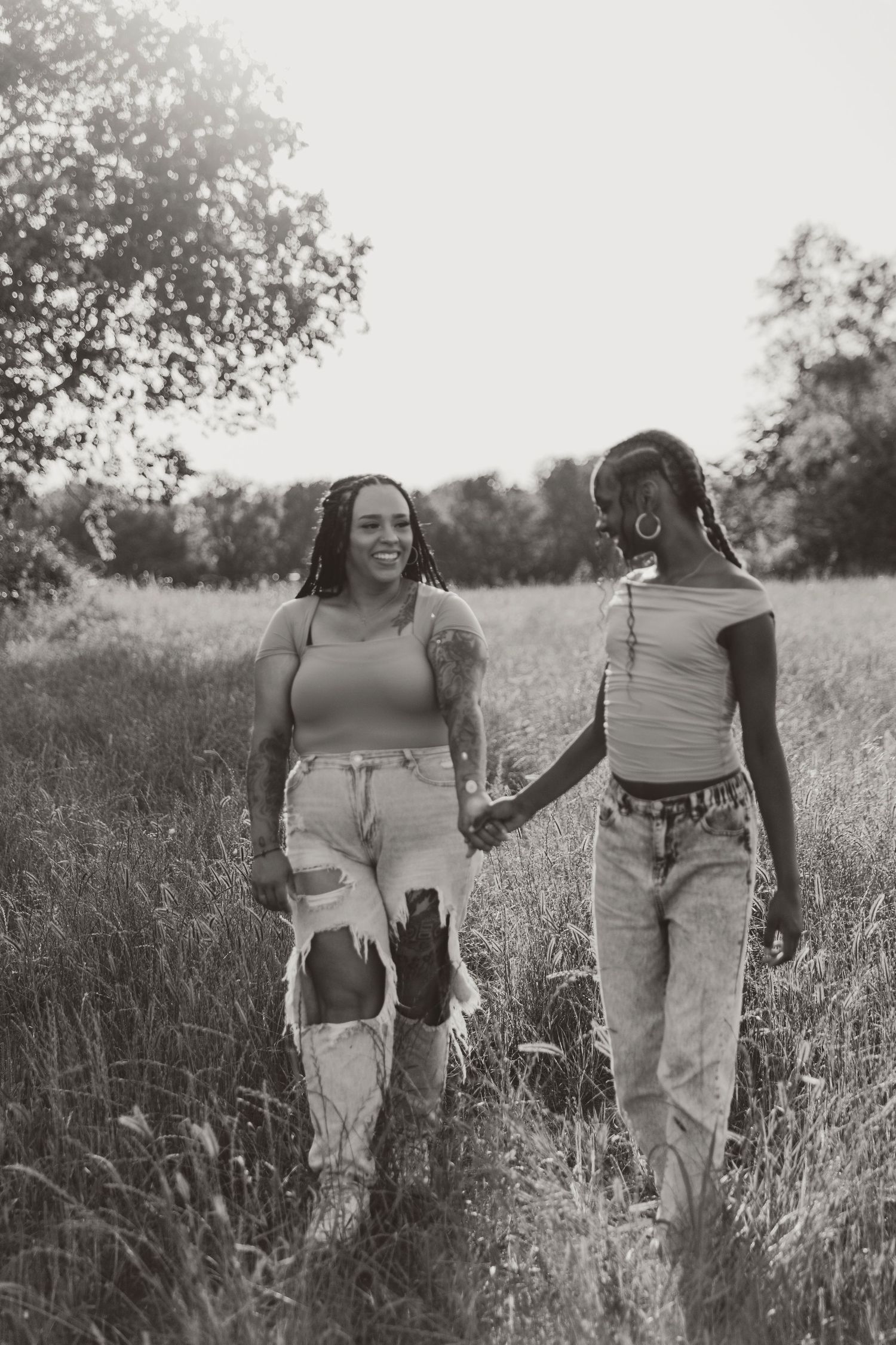 Two people walking hand in hand through tall grass during sunset.