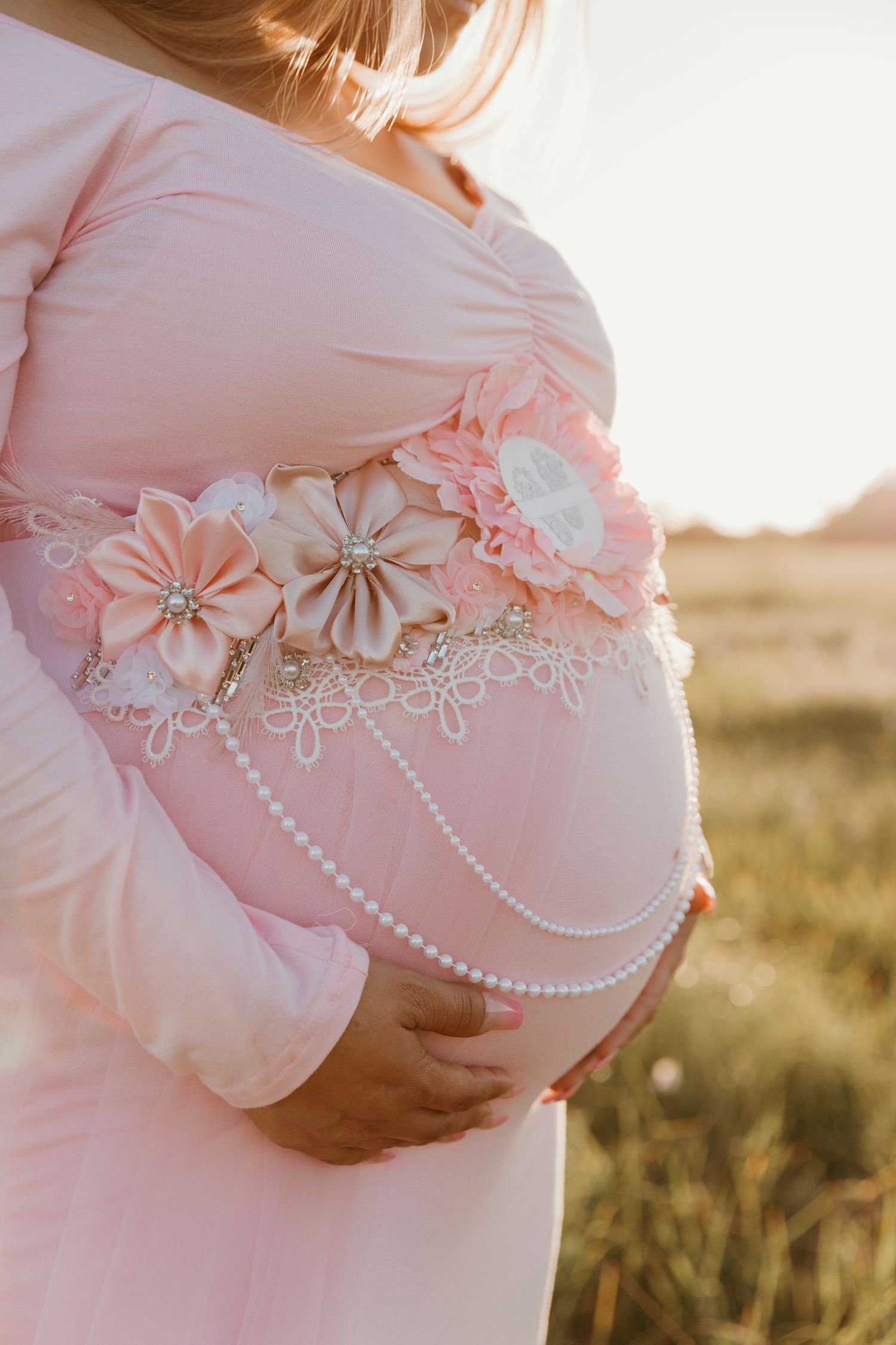 Close-up of a pregnant belly adorned with pink flowers and pearl details.