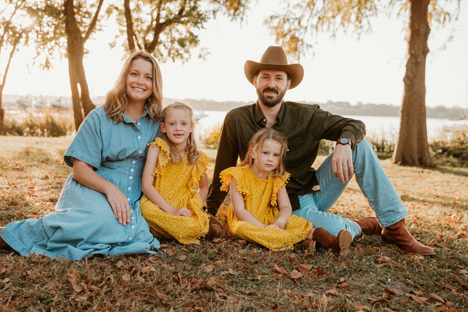 Family in coordinated yellow and blue outfits sitting together on grass during golden sunset photoshoot.