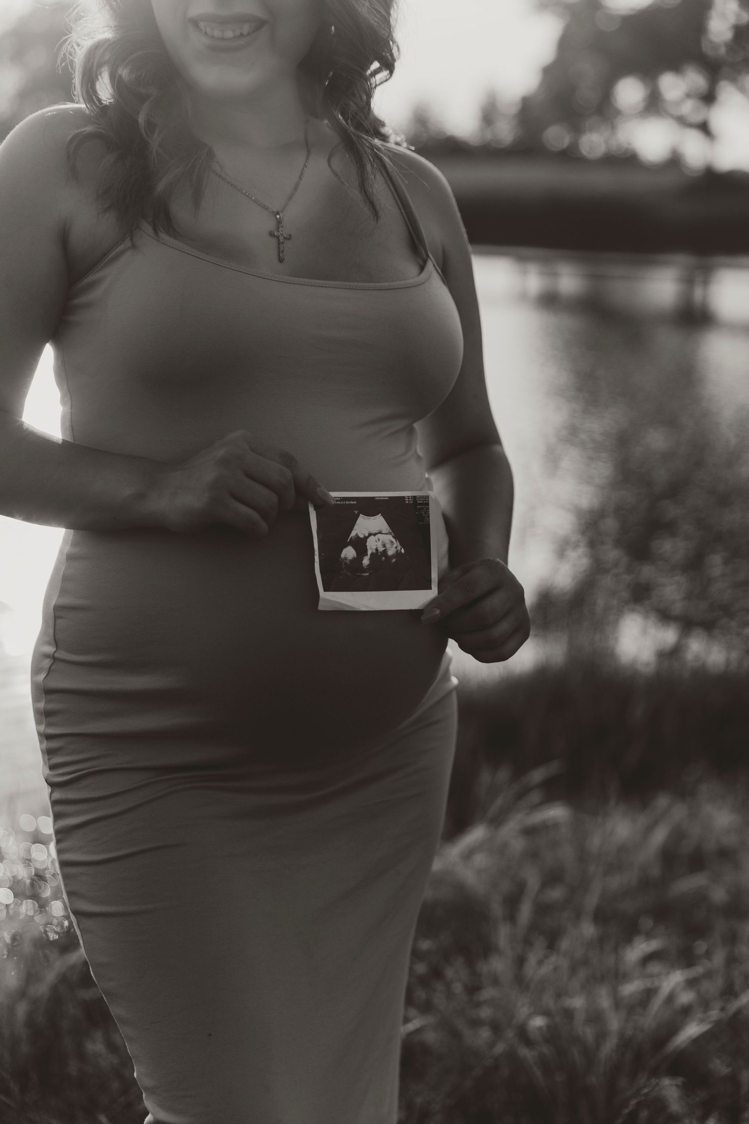Black and white maternity photo showing an ultrasound image in natural outdoor setting.