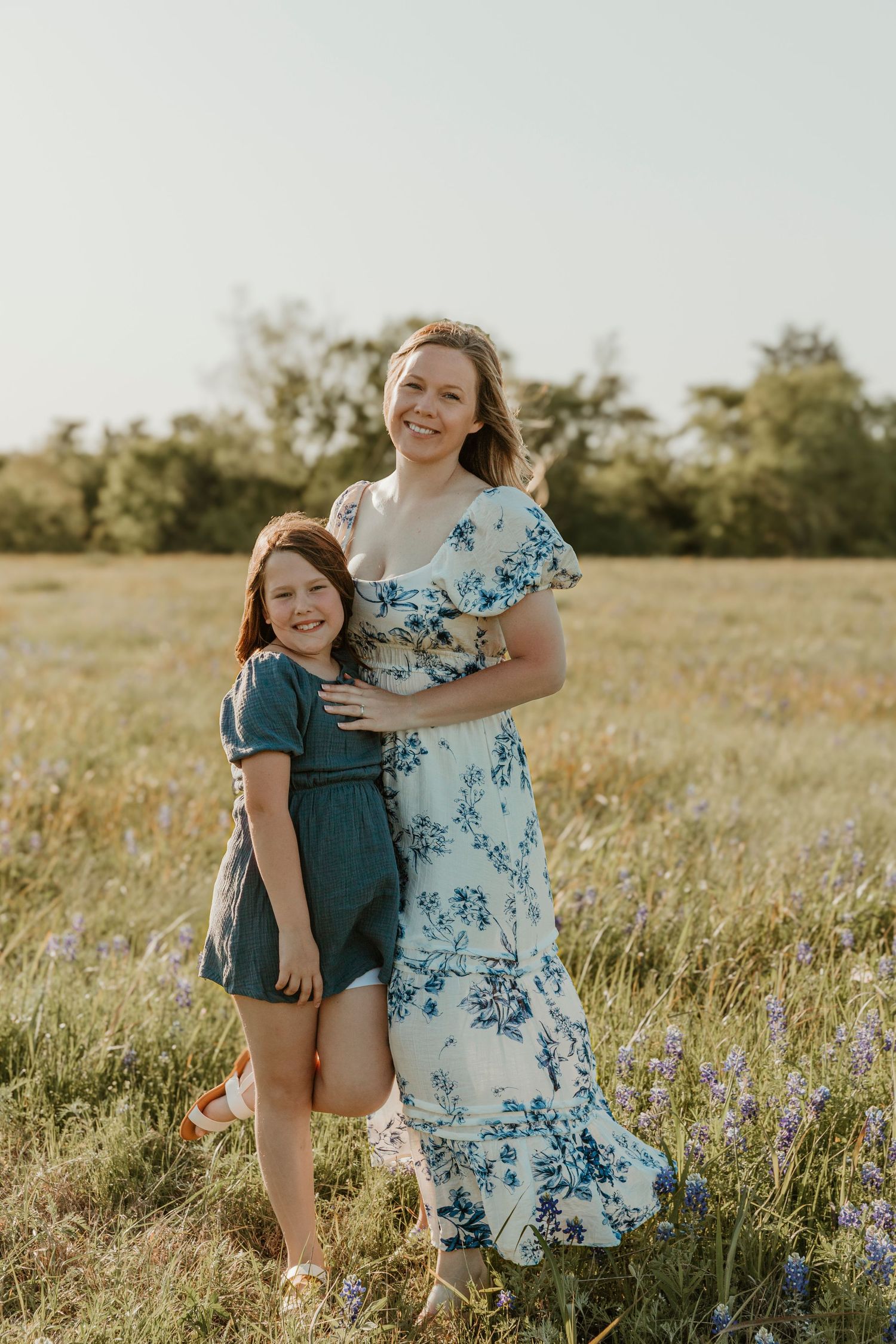 Candid family portrait in a sunny wildflower field with flowing blue floral dress.