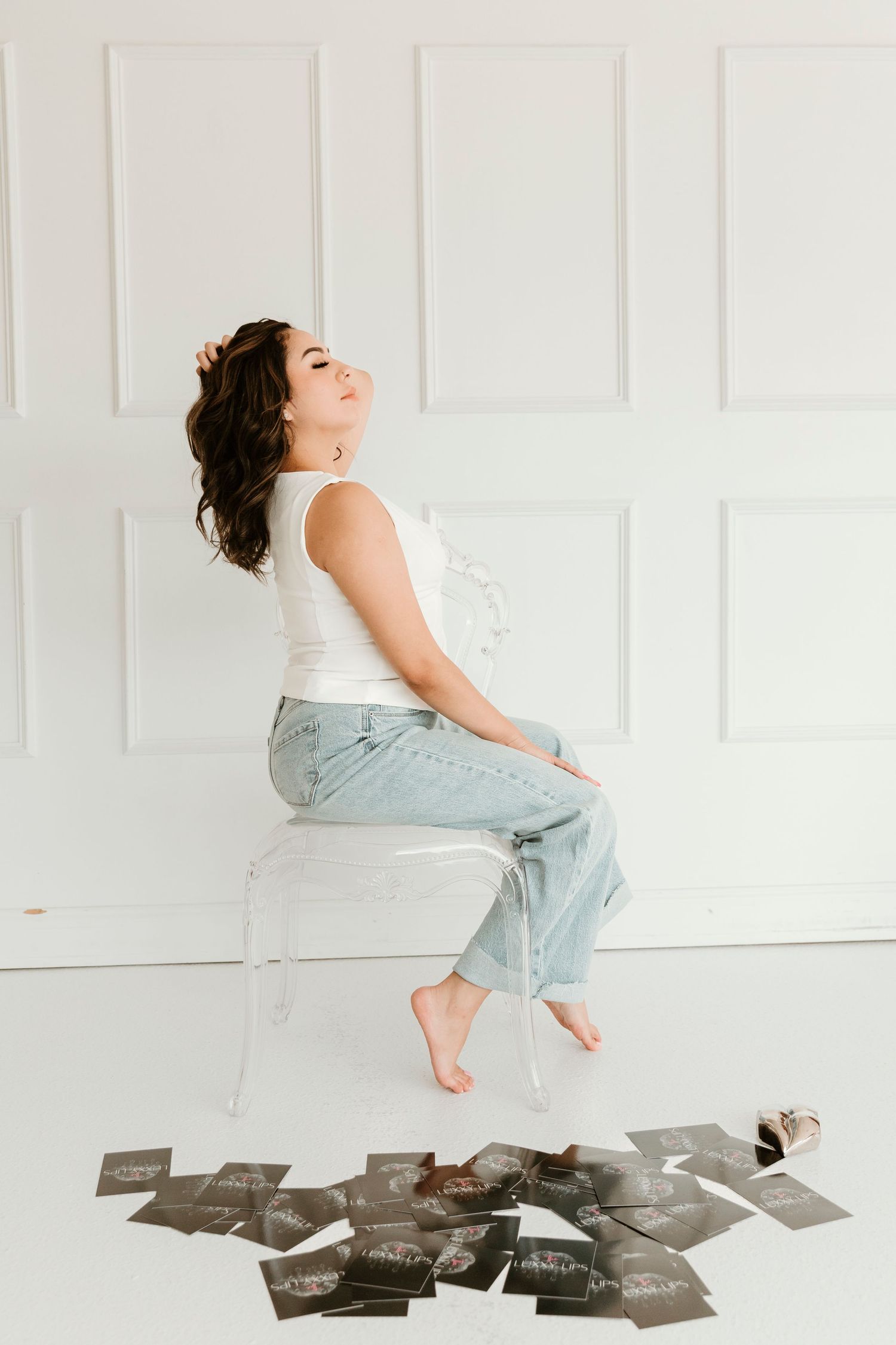 A person in white top and light jeans sits on scattered black and white photographs on a white floor.
