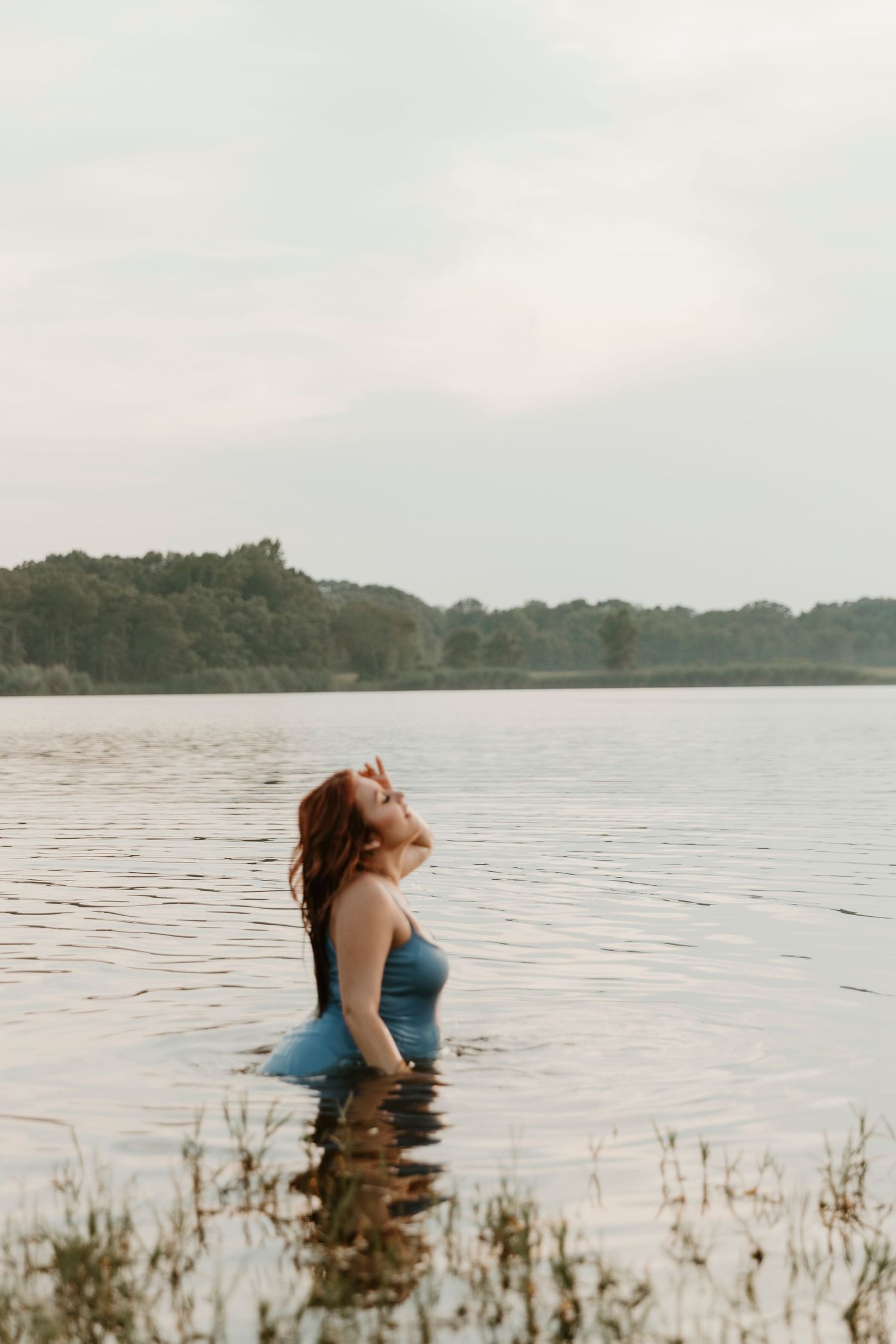 Person standing in lake water at sunset with trees in background.