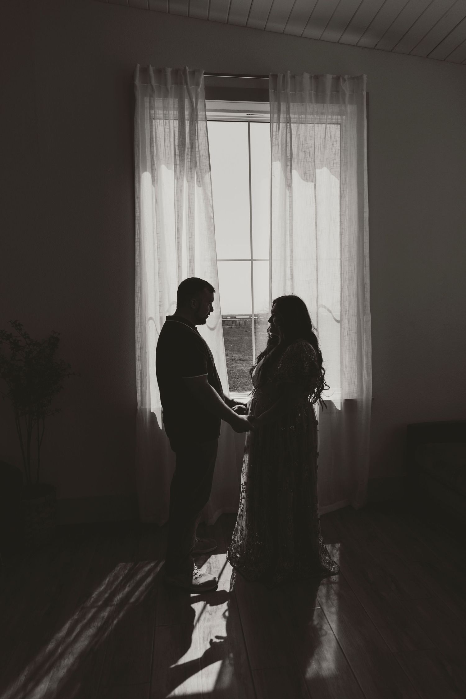 Silhouetted couple standing by a bright window in a minimalist room.