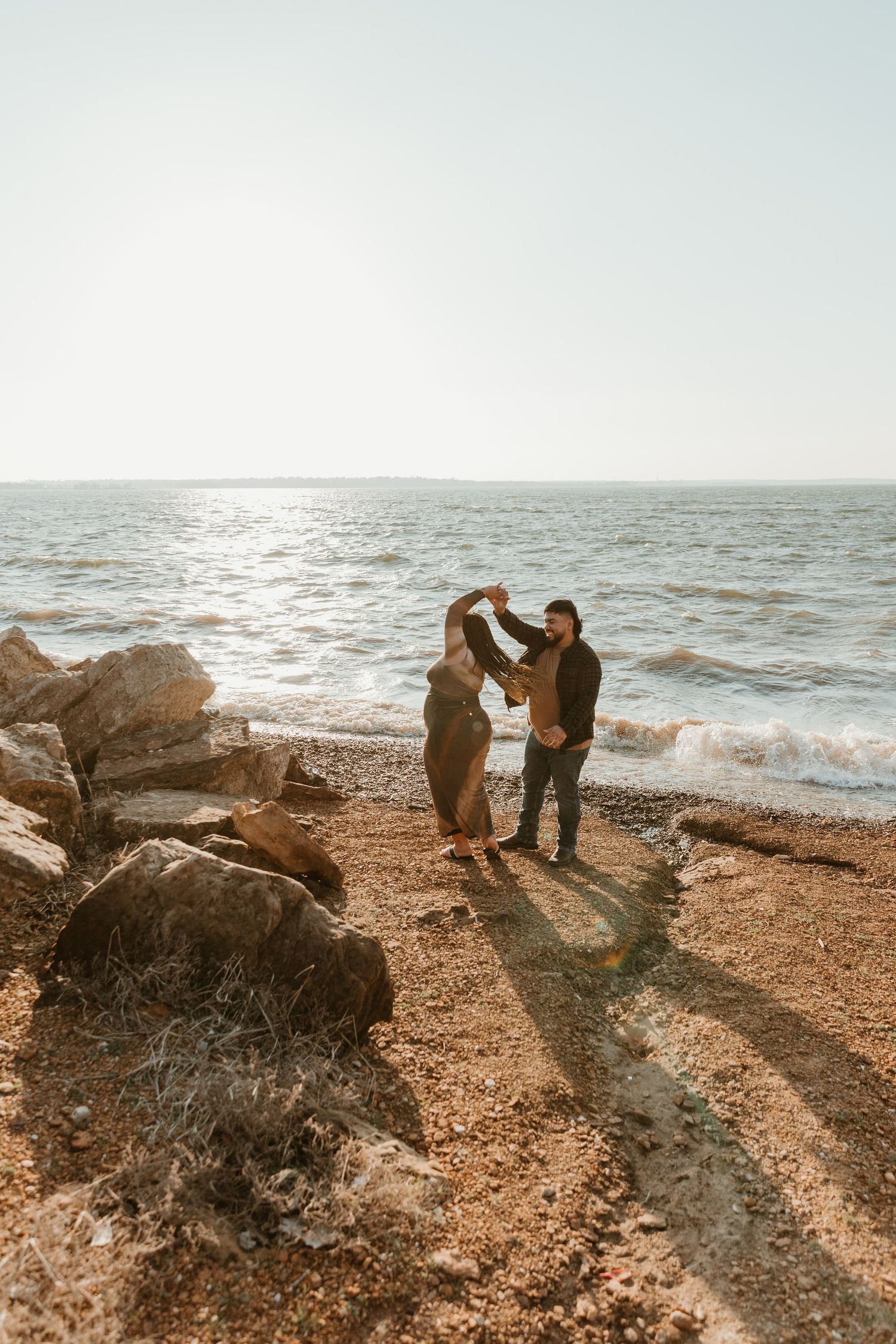 Silhouetted figures share an intimate moment on a rocky beach at golden hour.