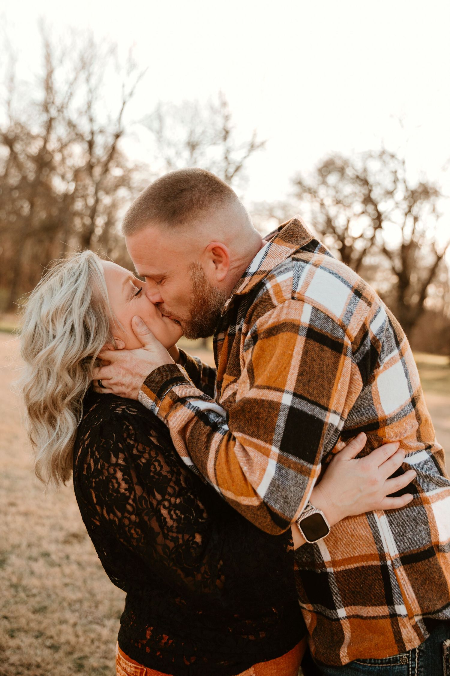 Romantic couple sharing an intimate kiss outdoors at sunset wearing fall clothing in a natural setting.