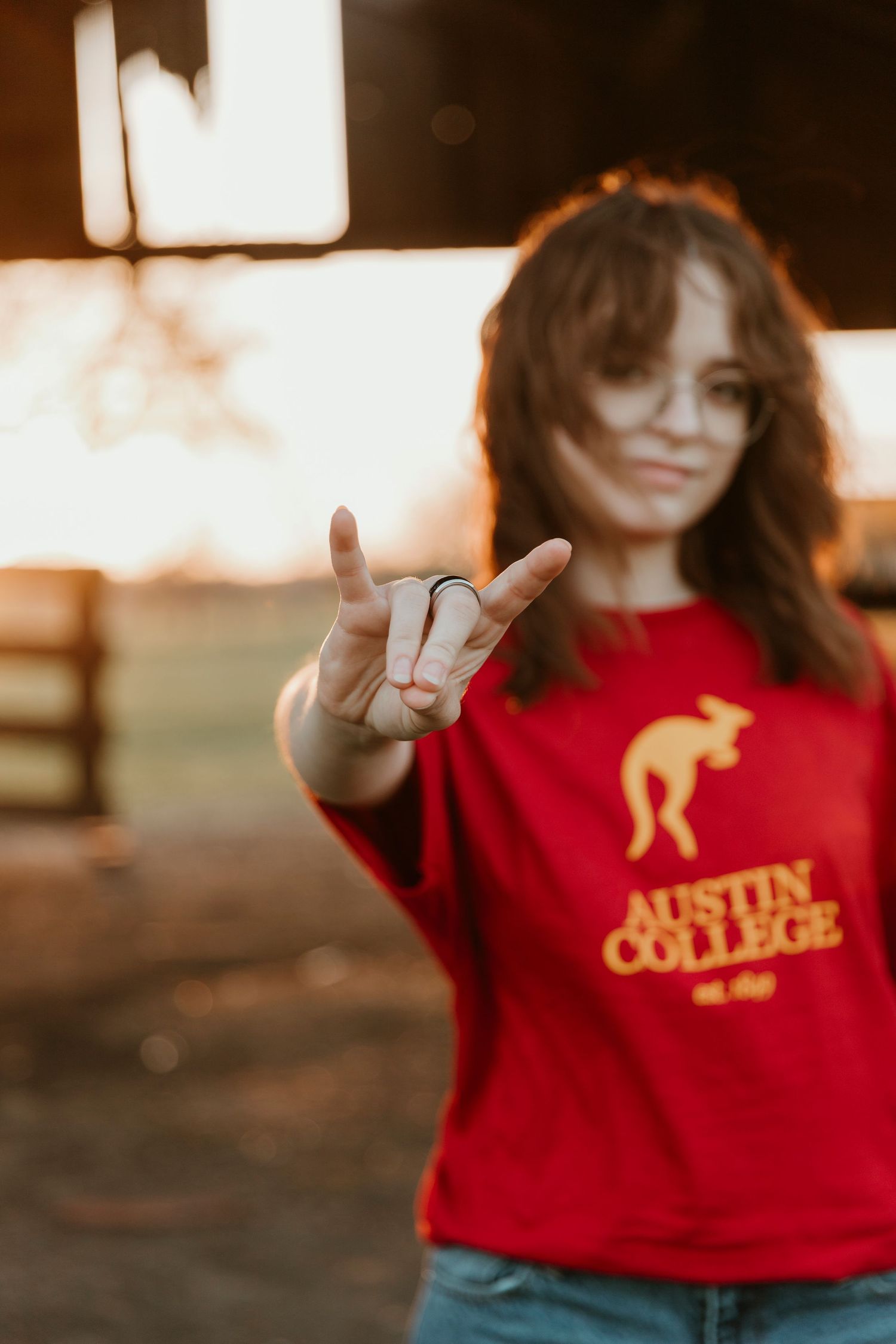 A red Austin College sweatshirt shown in golden hour light with peace sign gesture.