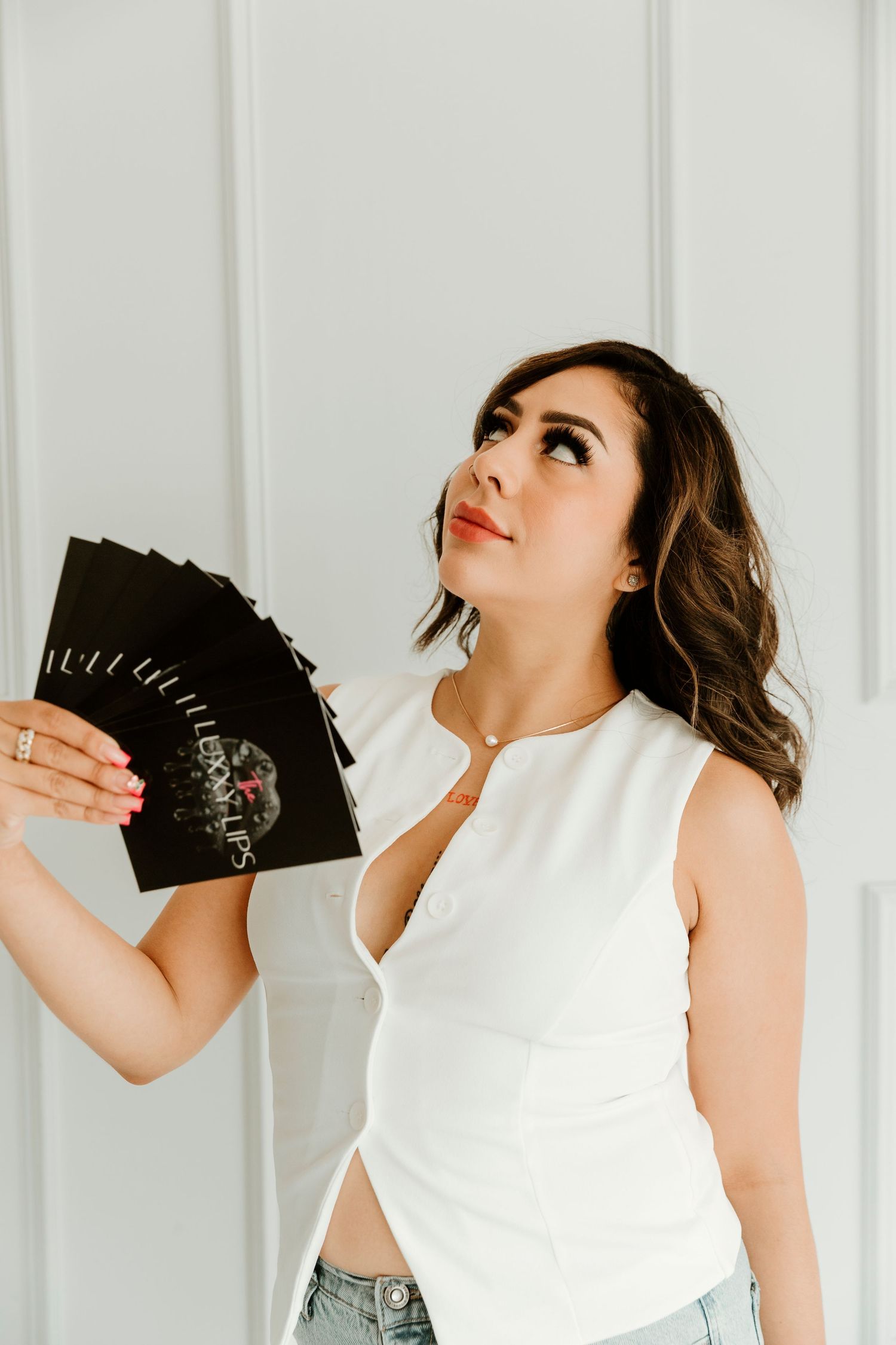 Person in white sleeveless top holds black cards while looking upward against white paneled wall.