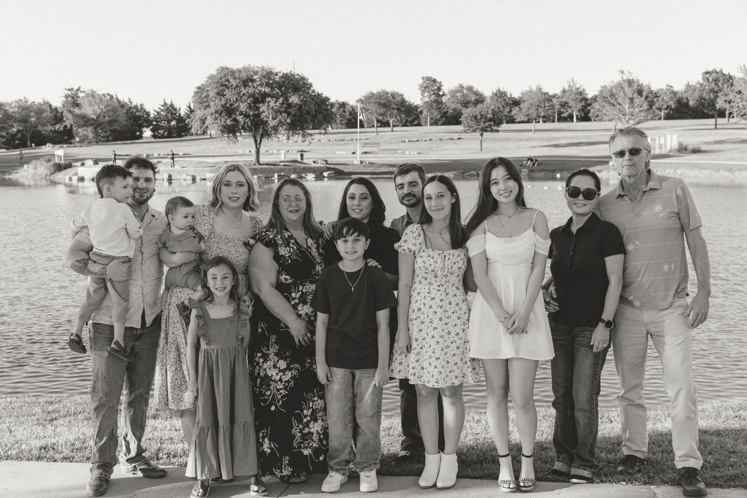 A large multi-generational family group poses together for a black and white photo by a lake.