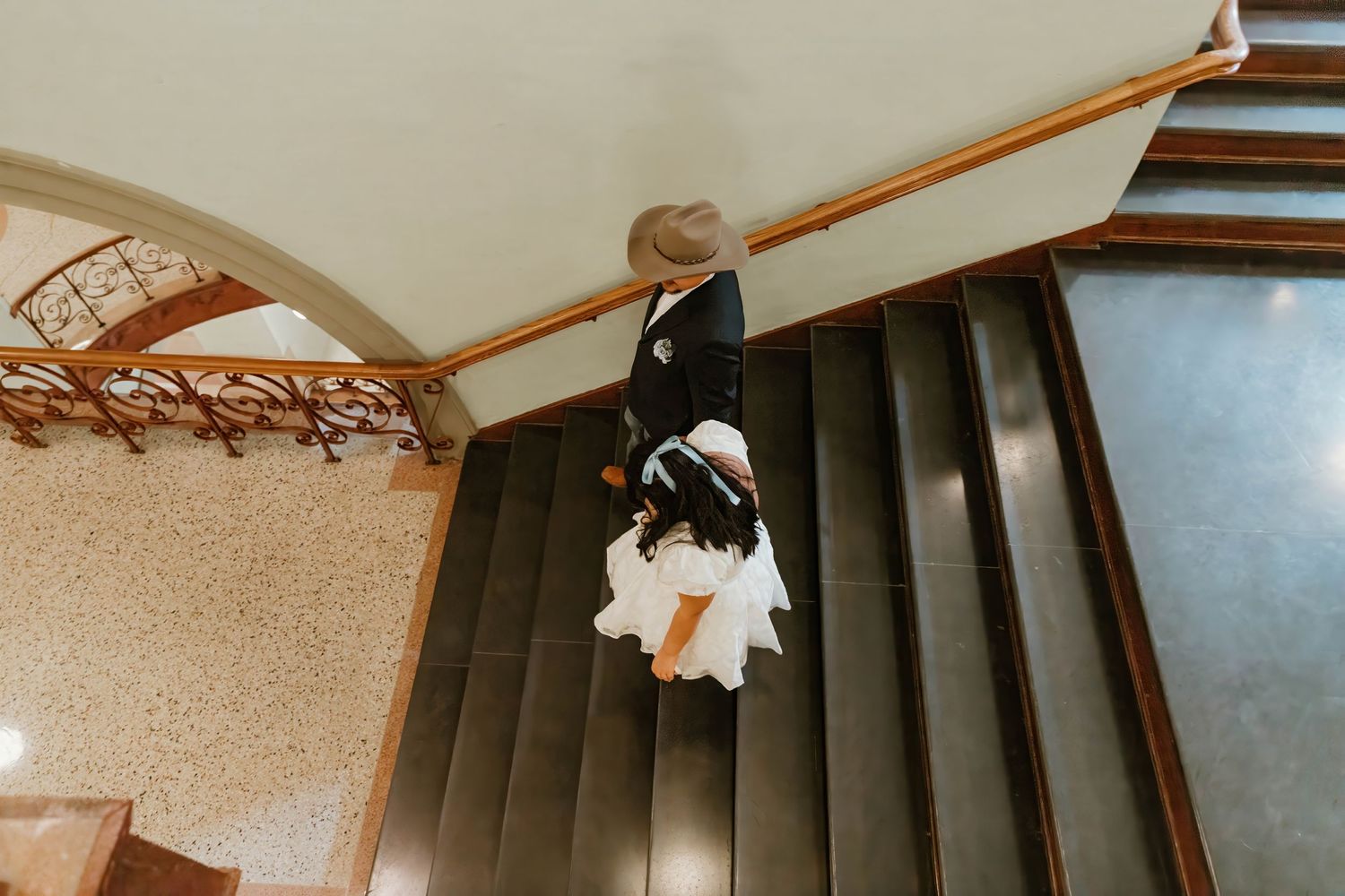 Wedding couple descending elegant staircase with ornate architectural details.