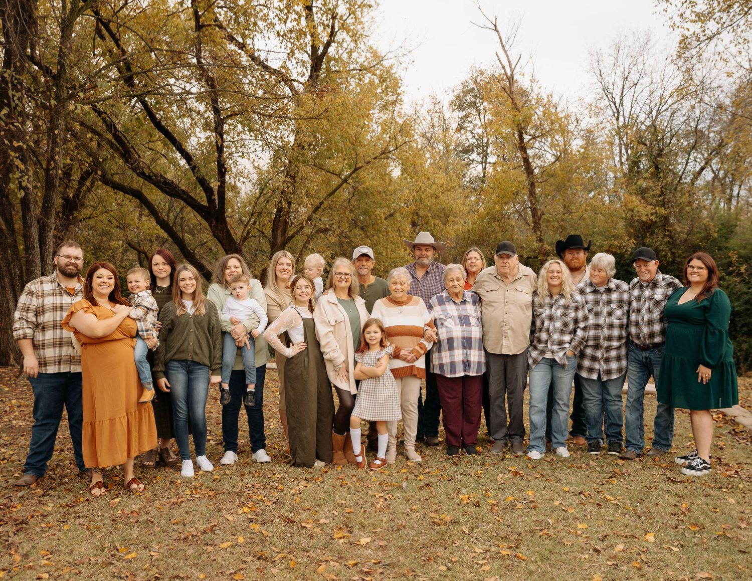Large family group posed outdoors in autumn with fall foliage and trees in the background.