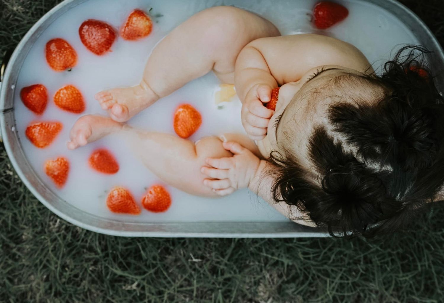 Bath photo with scattered heart-shaped strawberries floating in milky water.