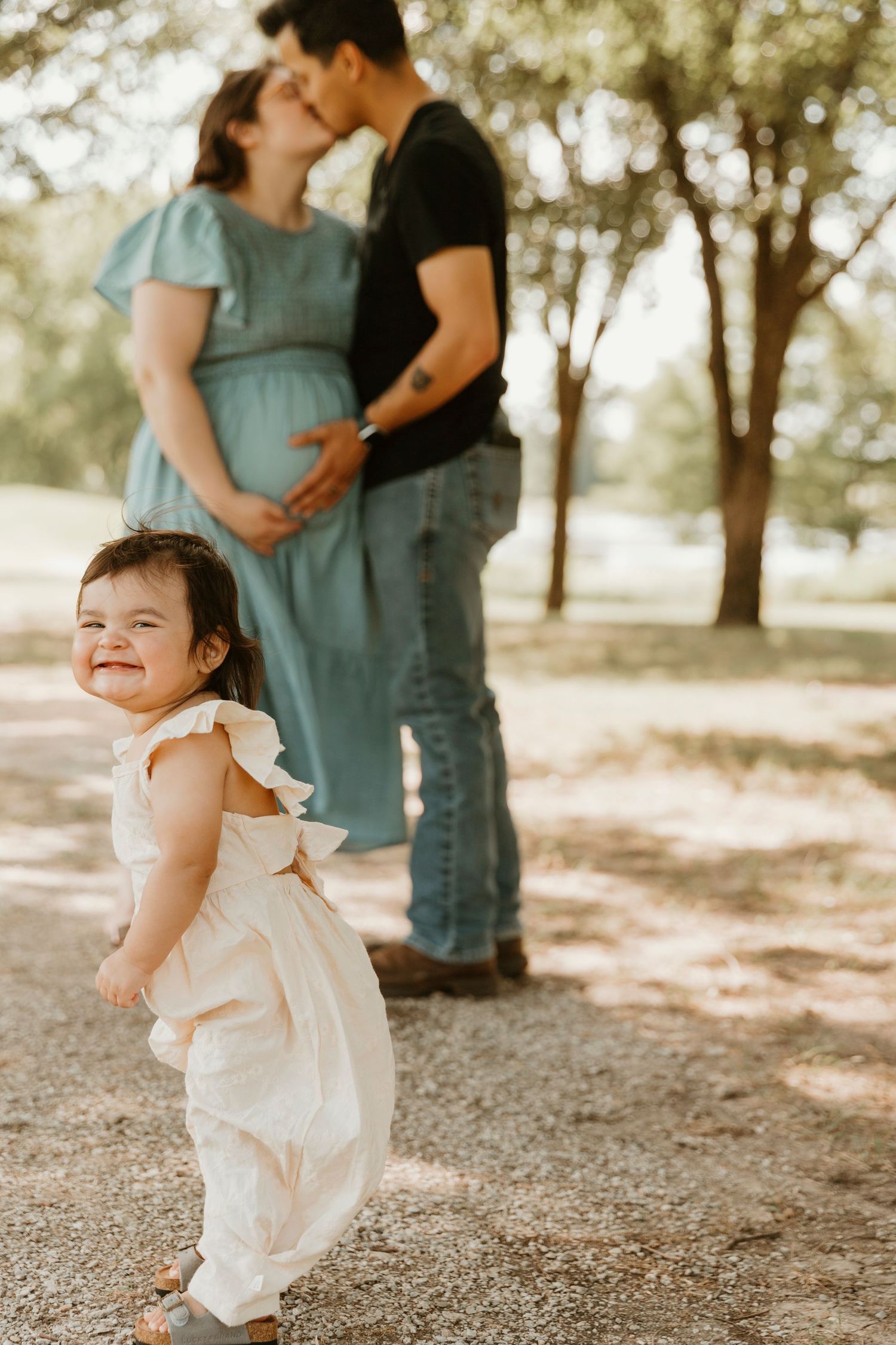 Playful family maternity photo with toddler smiling in foreground.