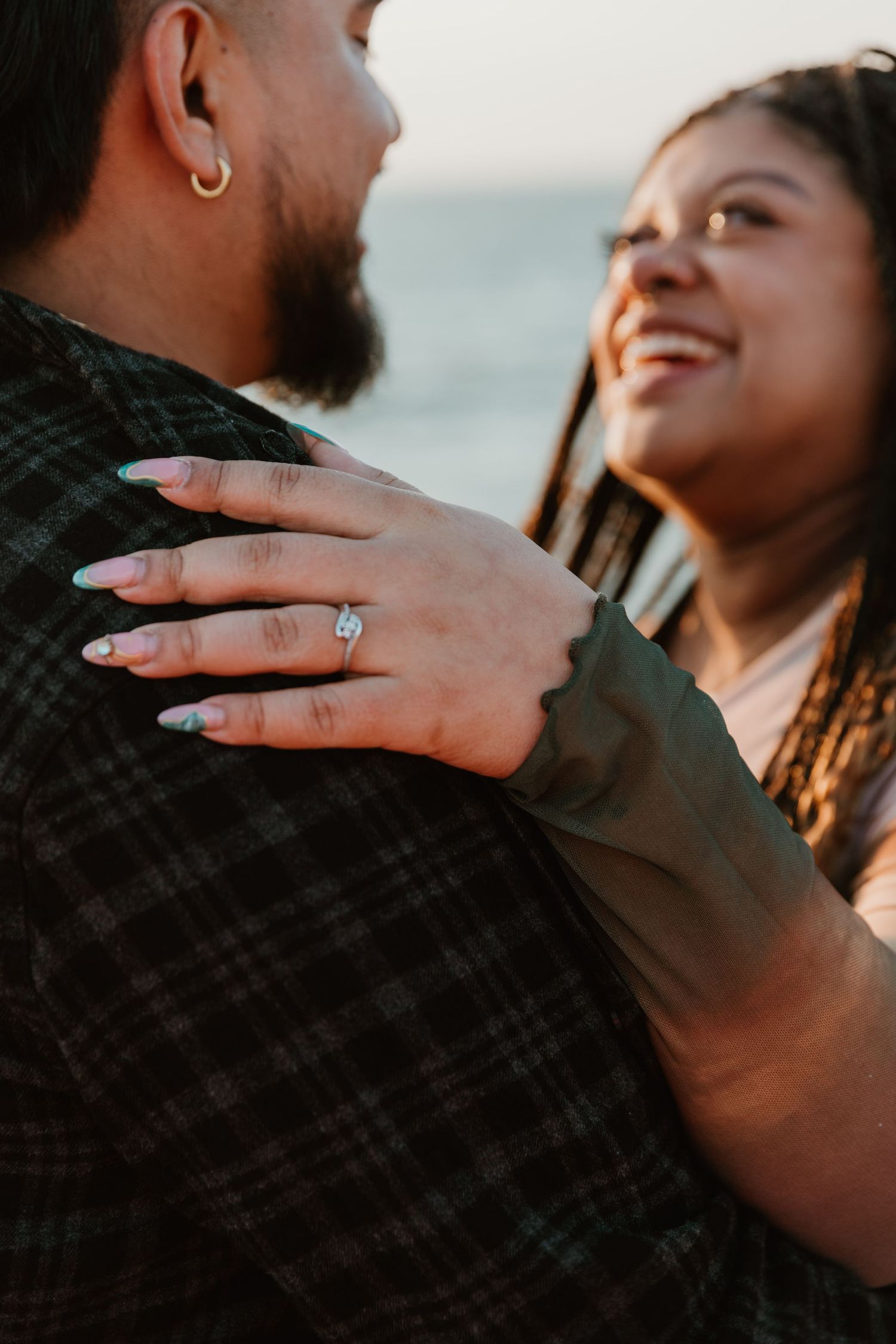 Close-up engagement ring shot during intimate seaside photo session.