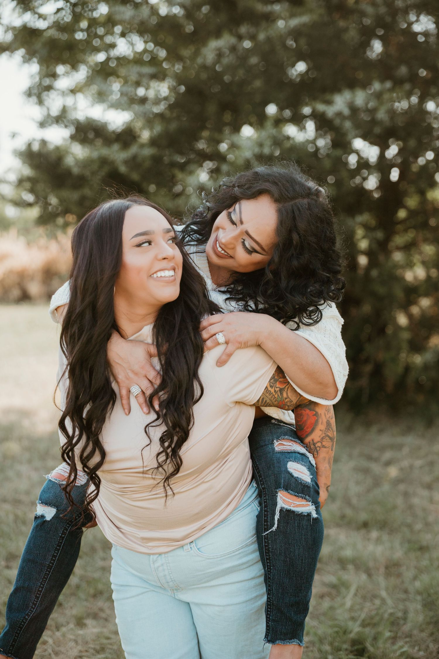 Two smiling women embracing outdoors, one giving the other a piggyback ride.