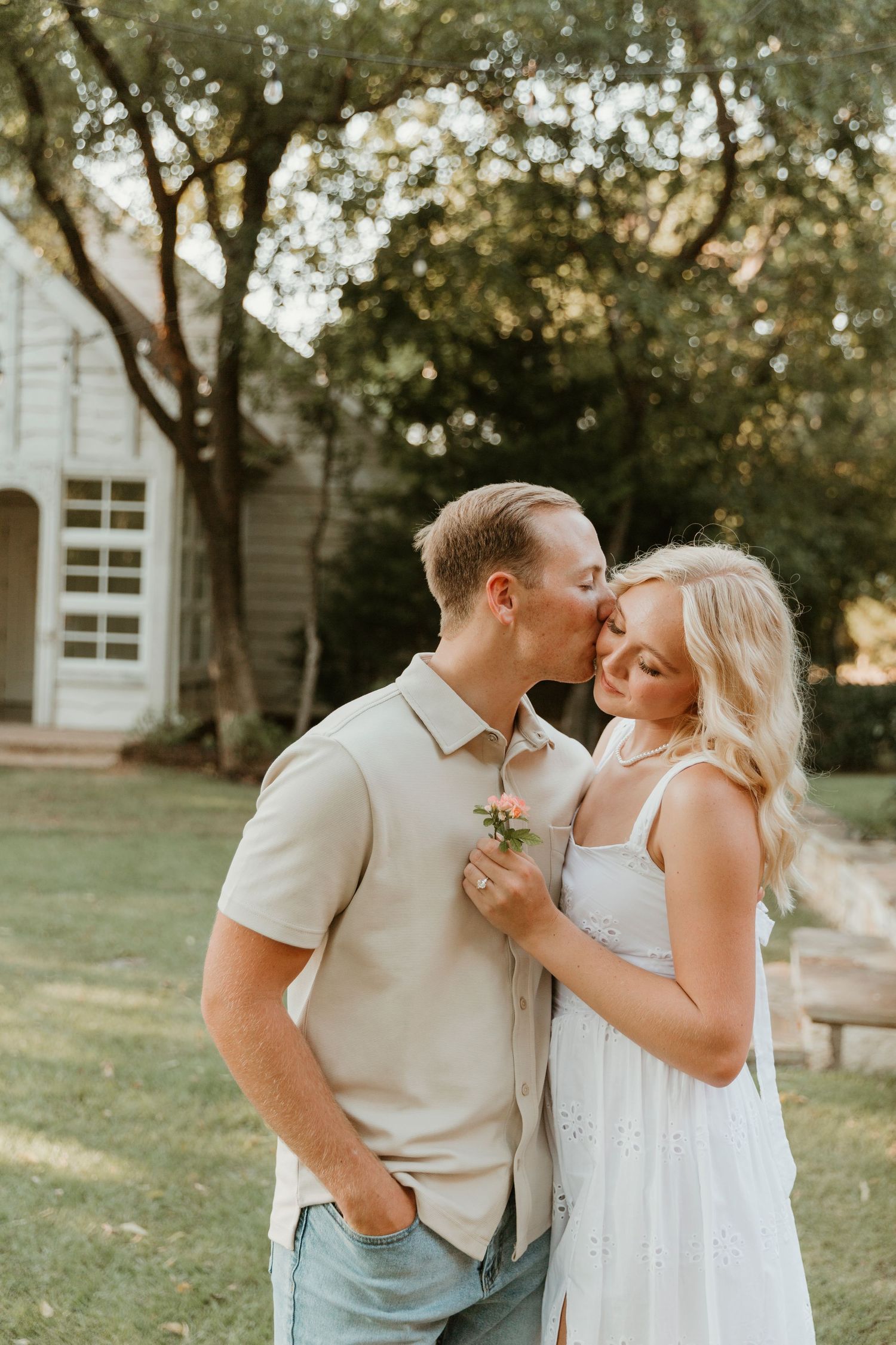 A tender moment captured between a couple in casual attire against a garden church setting.