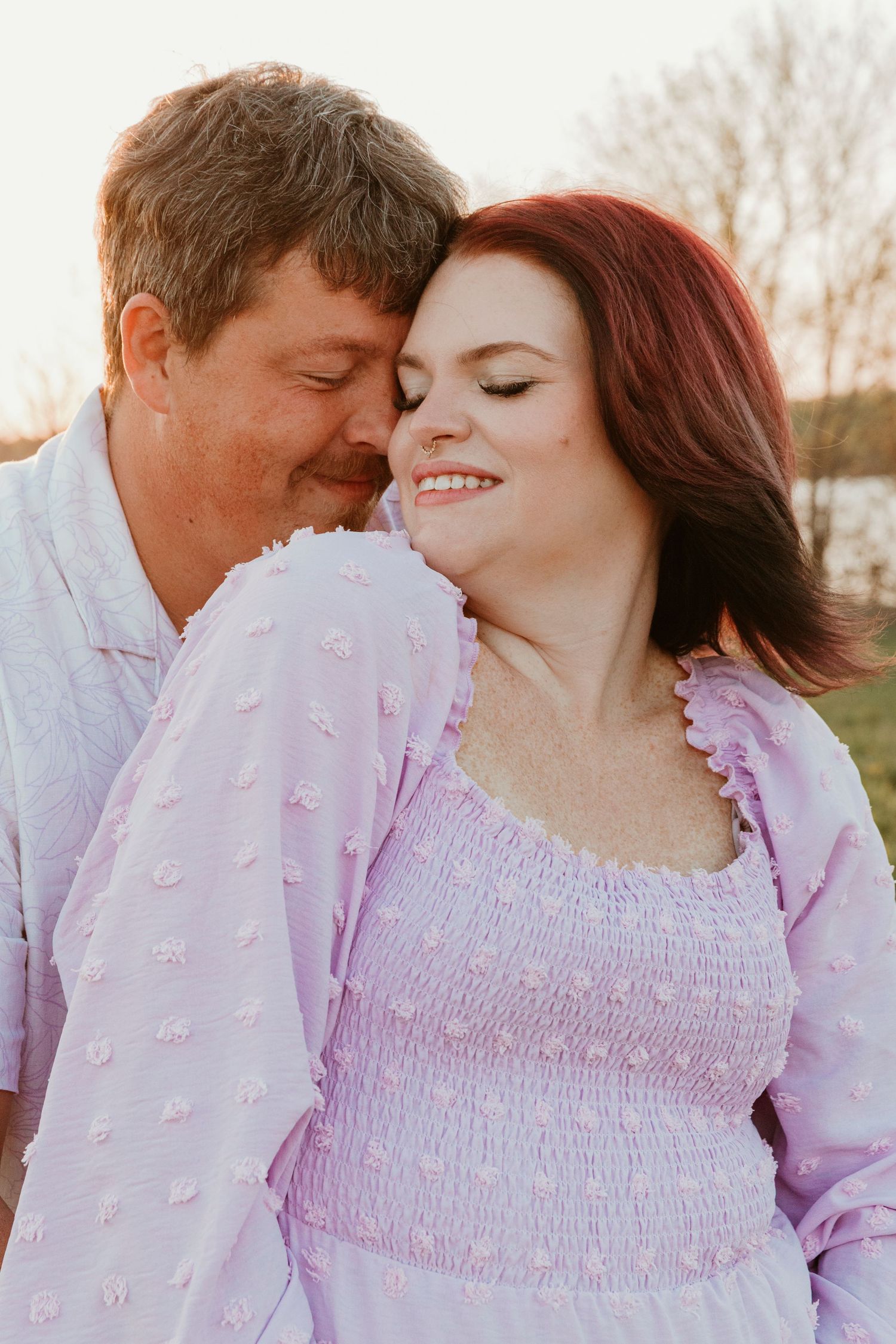 A romantic couple embraces in soft lighting wearing pink and white outfits.