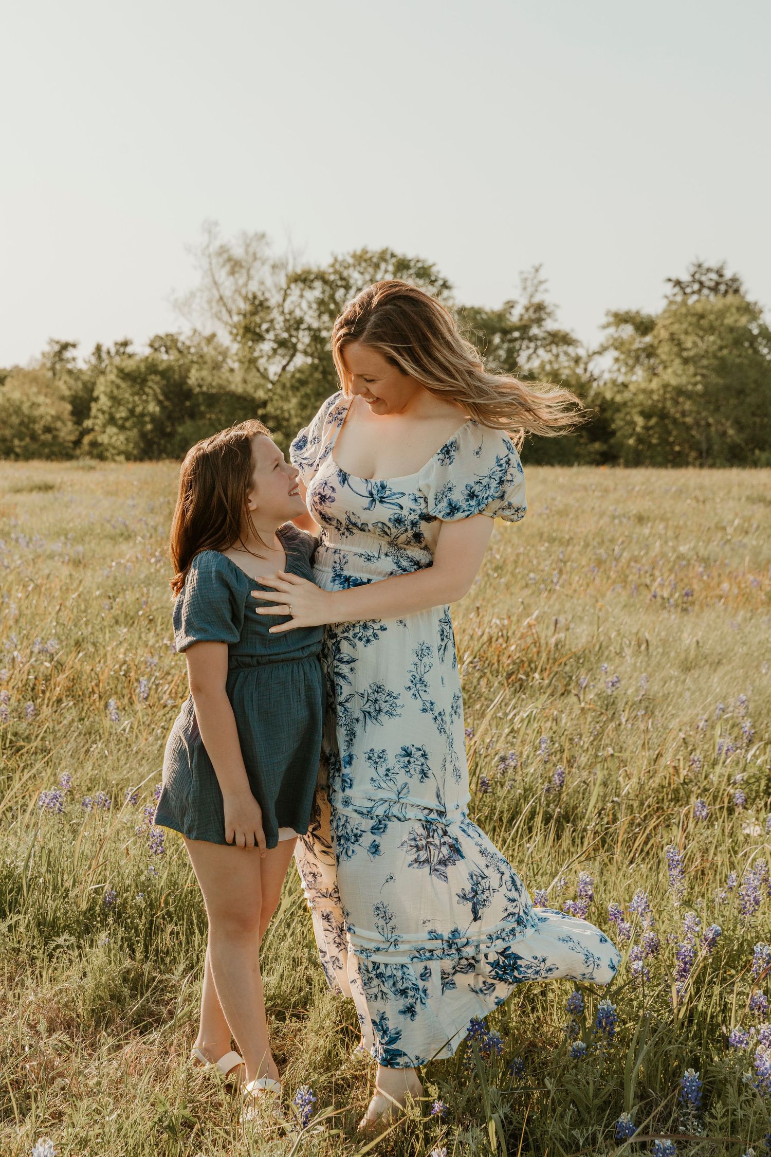 Playful interaction between family members in a field with blue wildflowers at sunset.