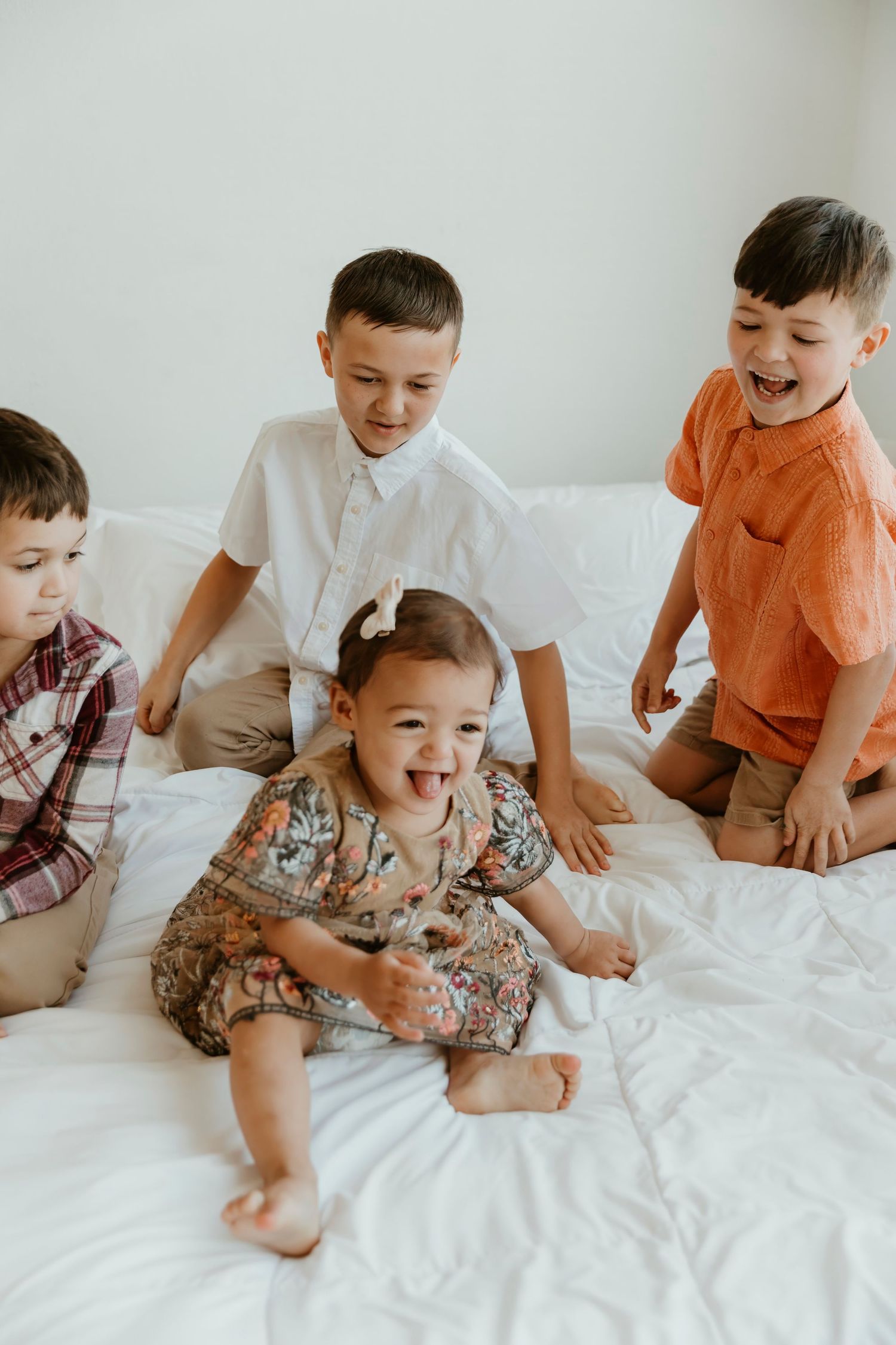 Four children laughing and playing together on white bedding.