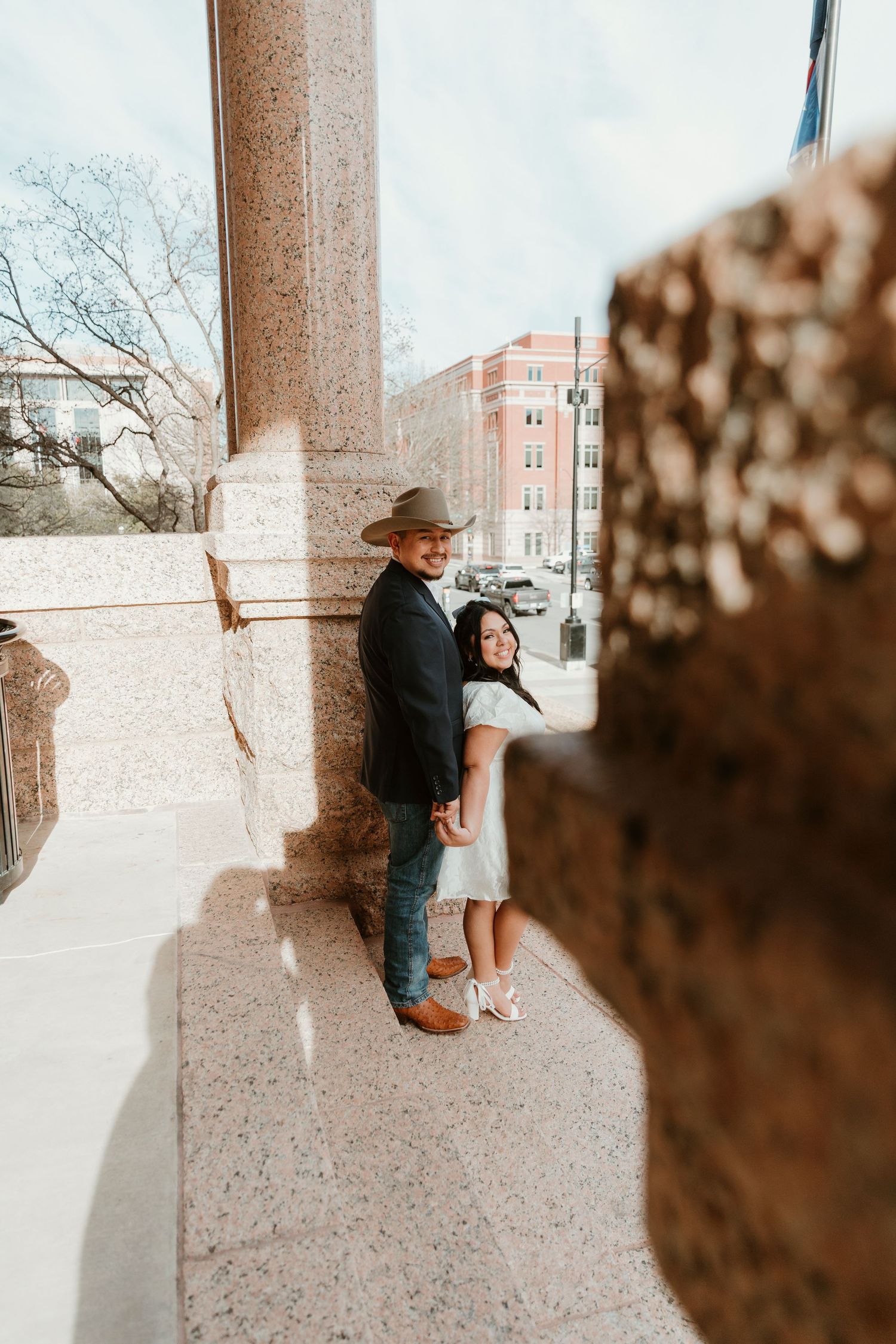 Romantic scene against stone columns with urban architecture in the background.