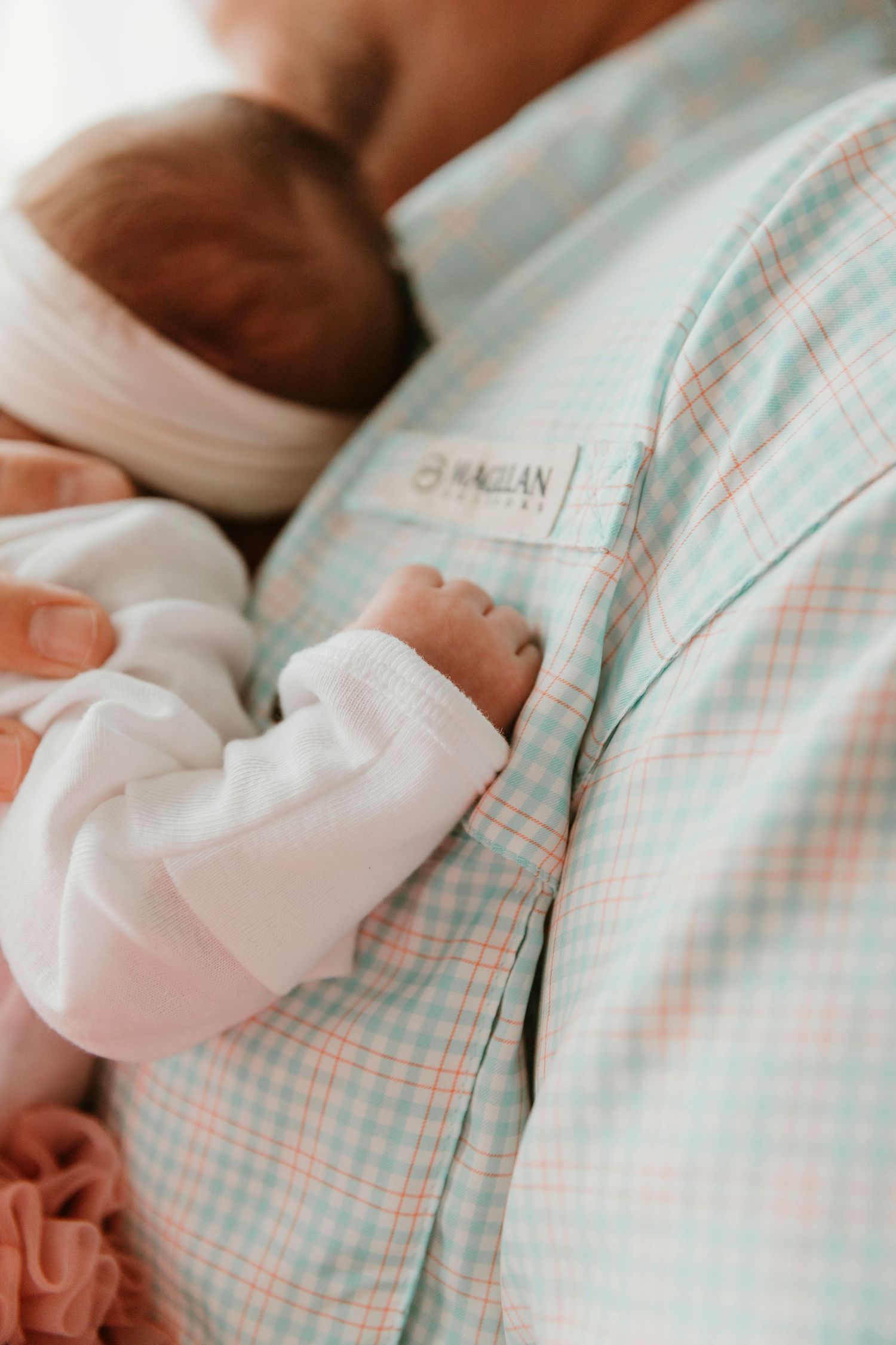 Newborn baby resting against parent wearing plaid shirt.