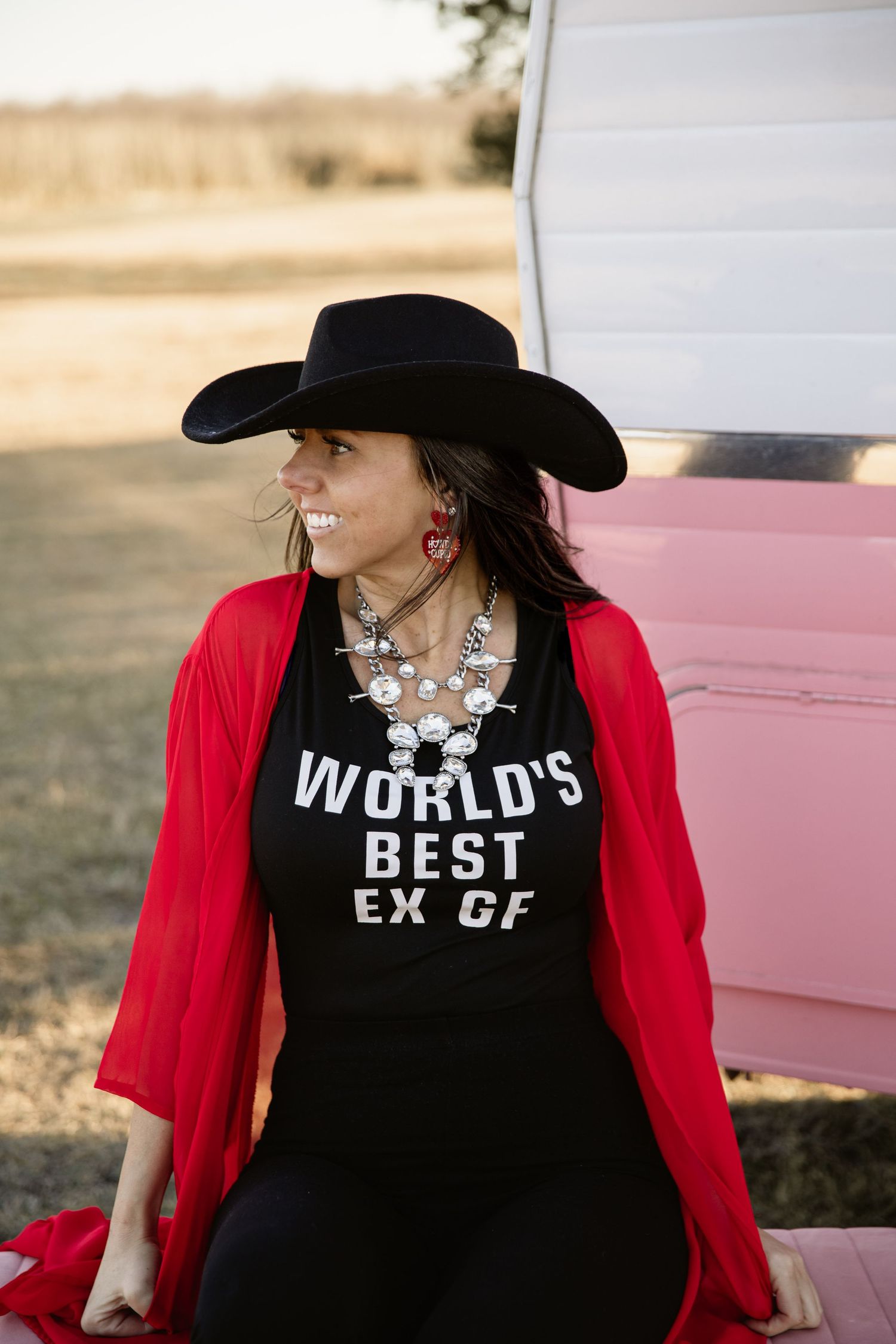 Person wearing black t-shirt with text and red cardigan posing near pink vehicle.