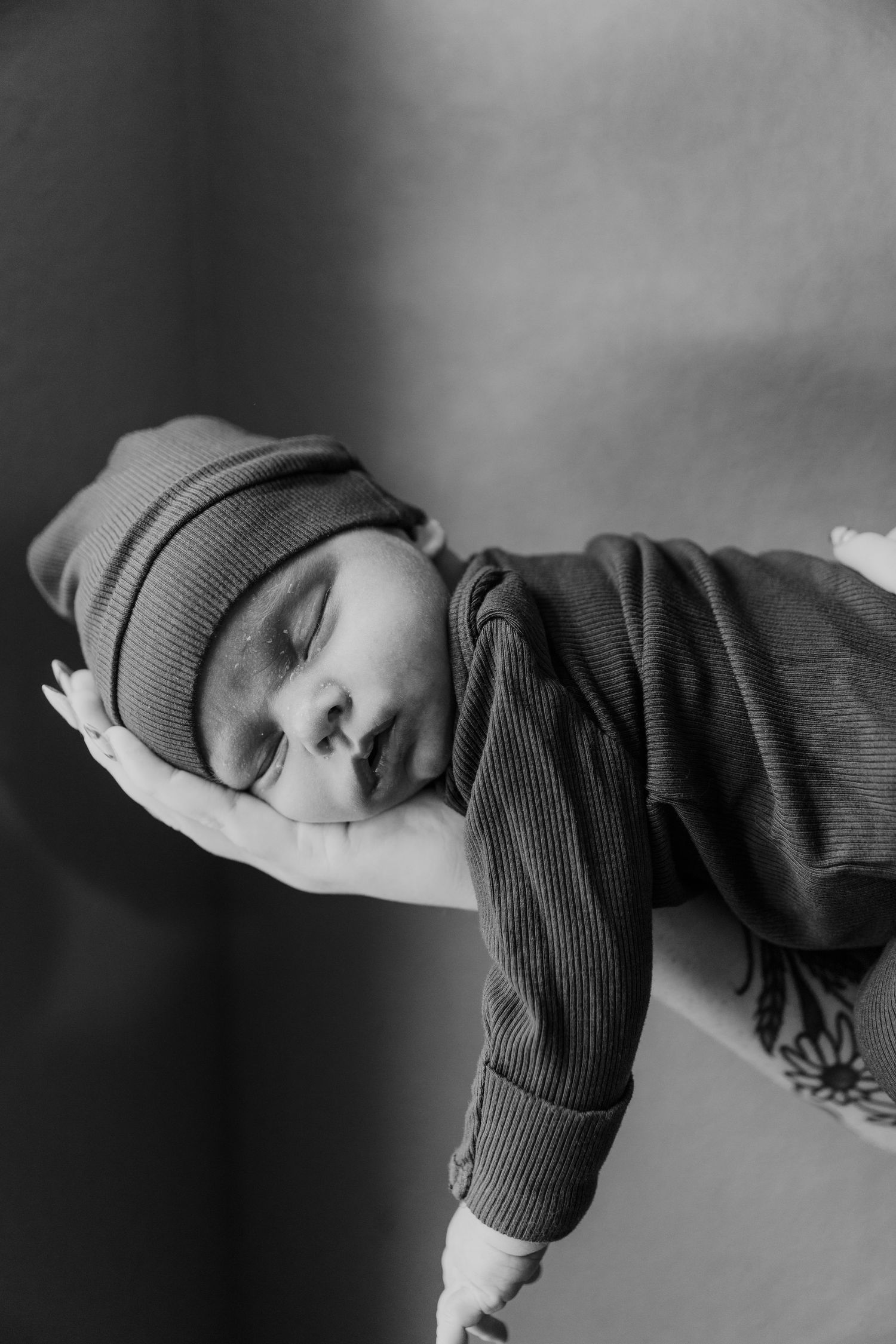 A sleeping infant wearing a gray knit beanie and striped shirt rests peacefully in black and white.