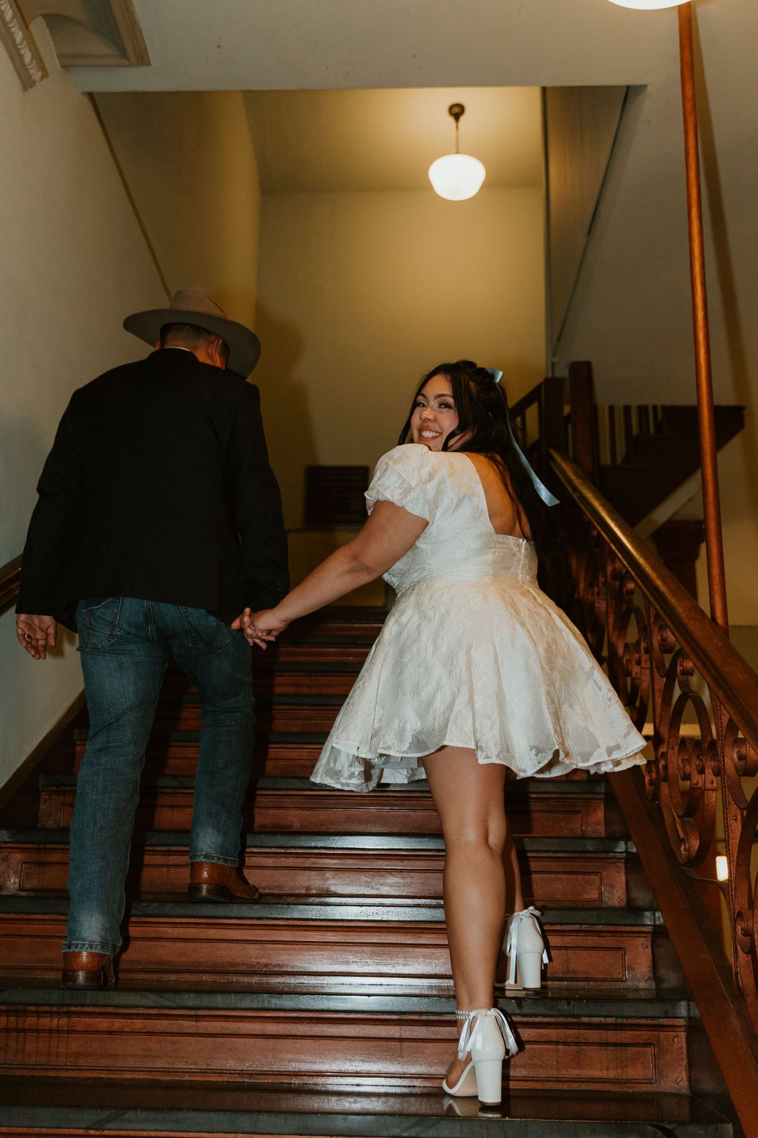 People ascending wooden stairs in formal wear with white dress and cowboy boots visible.