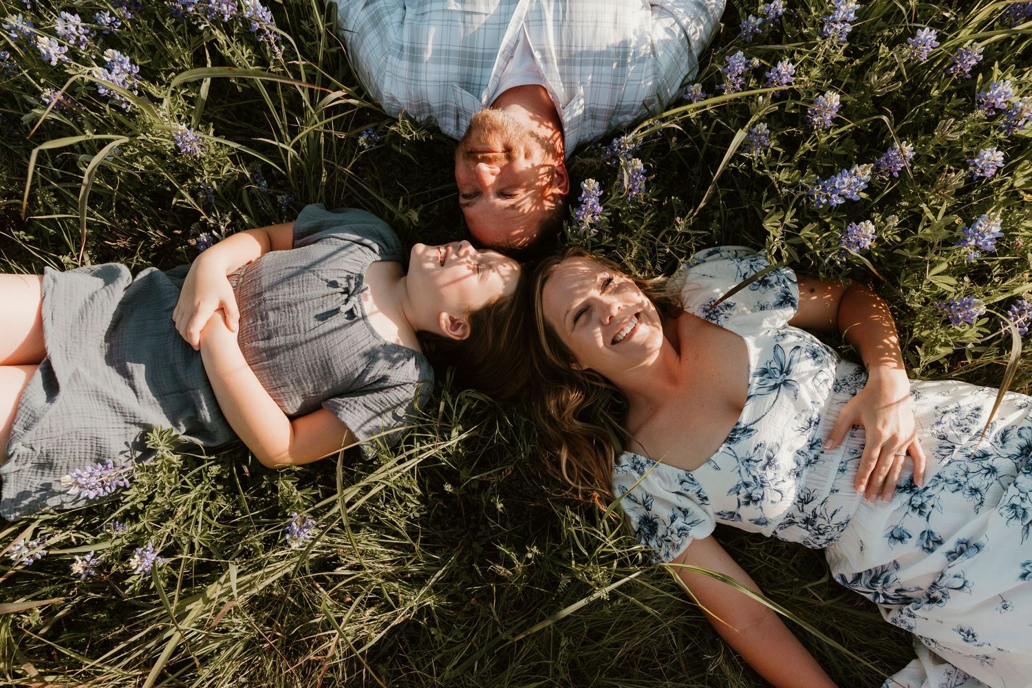 Family lying together in tall grass and wildflowers during outdoor photo session.