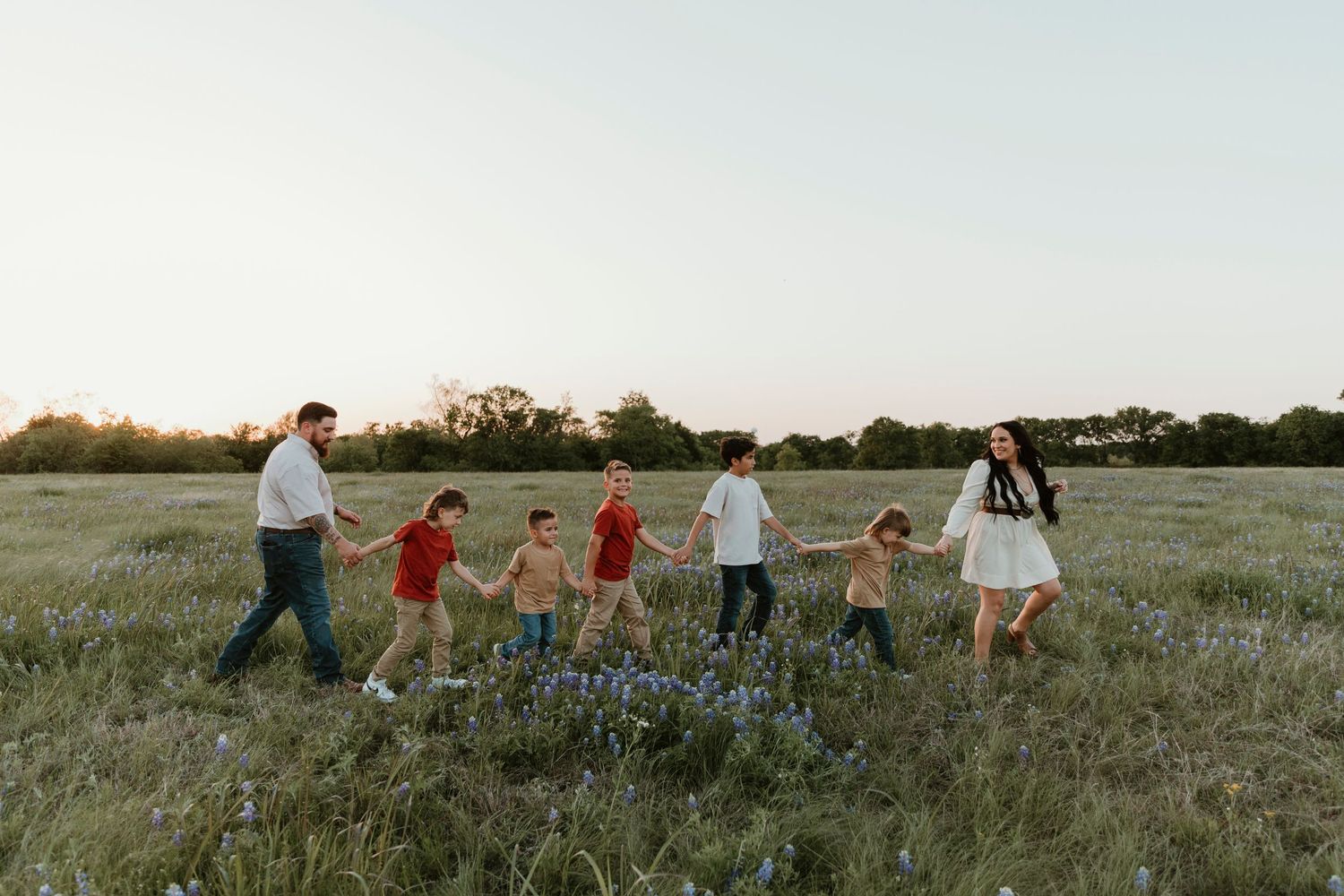 Wide landscape shot of a family walking through a field of wildflowers at dusk.
