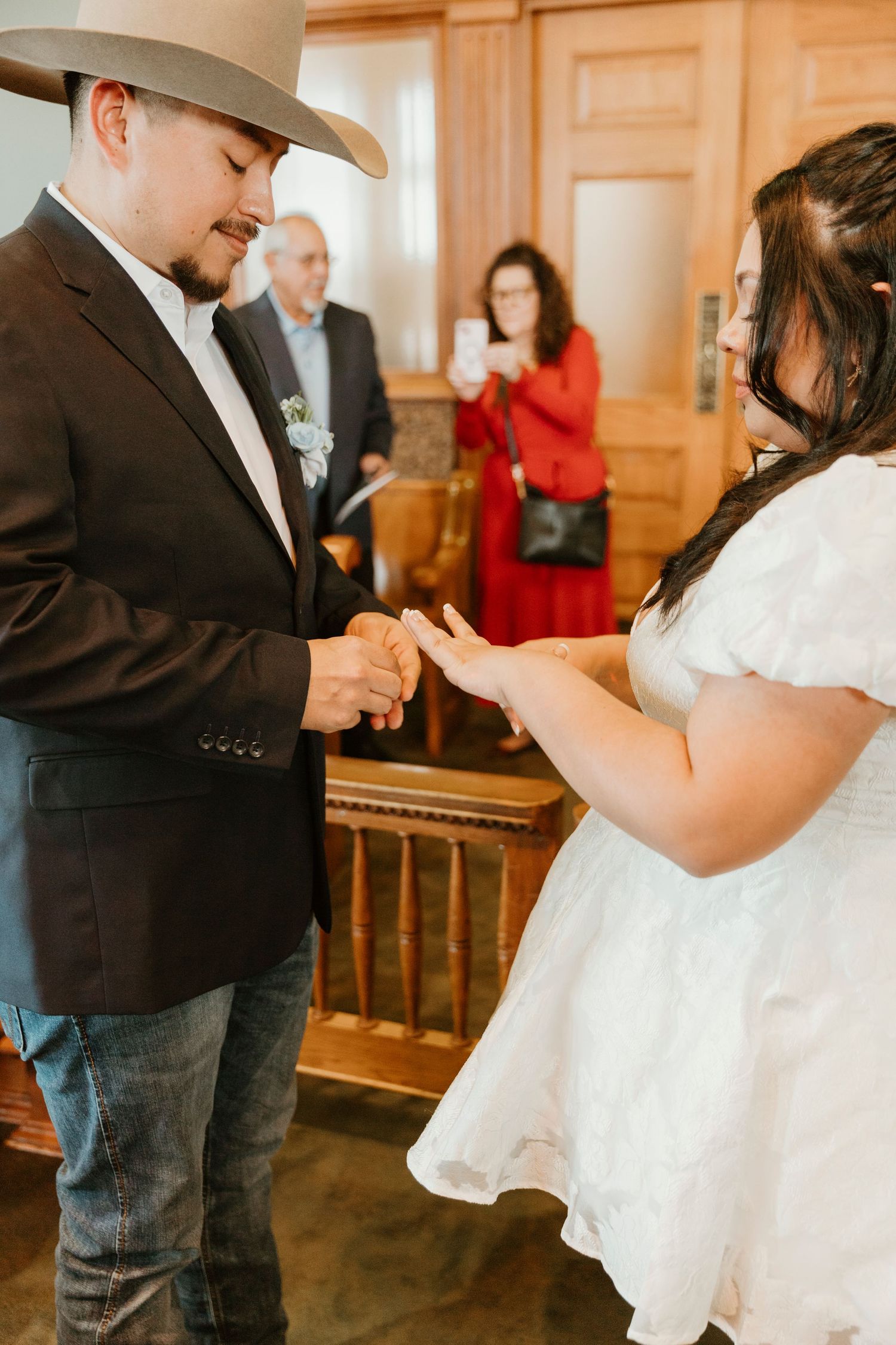 Couple exchanging rings during an intimate wedding ceremony in a rustic indoor setting.