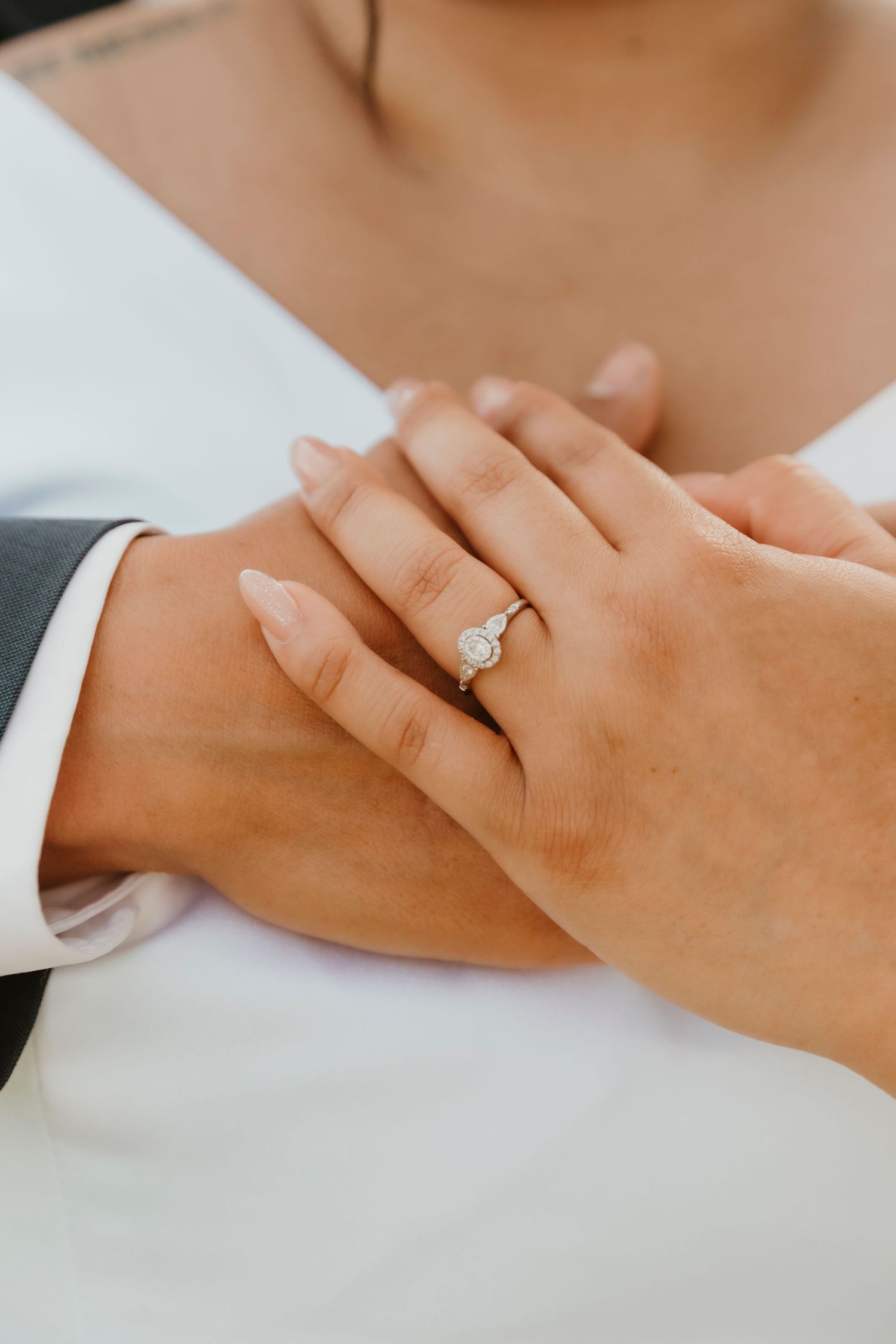 Close-up of hands with engagement ring against formal wedding attire.