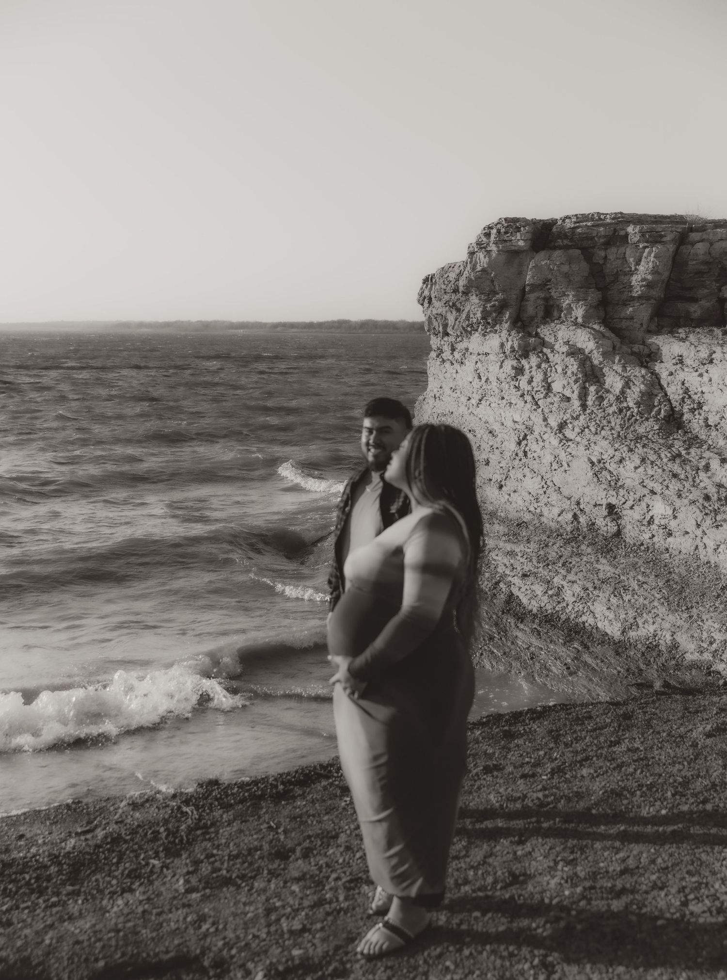 A maternity photoshoot silhouette against dramatic coastal cliffs and ocean waves.