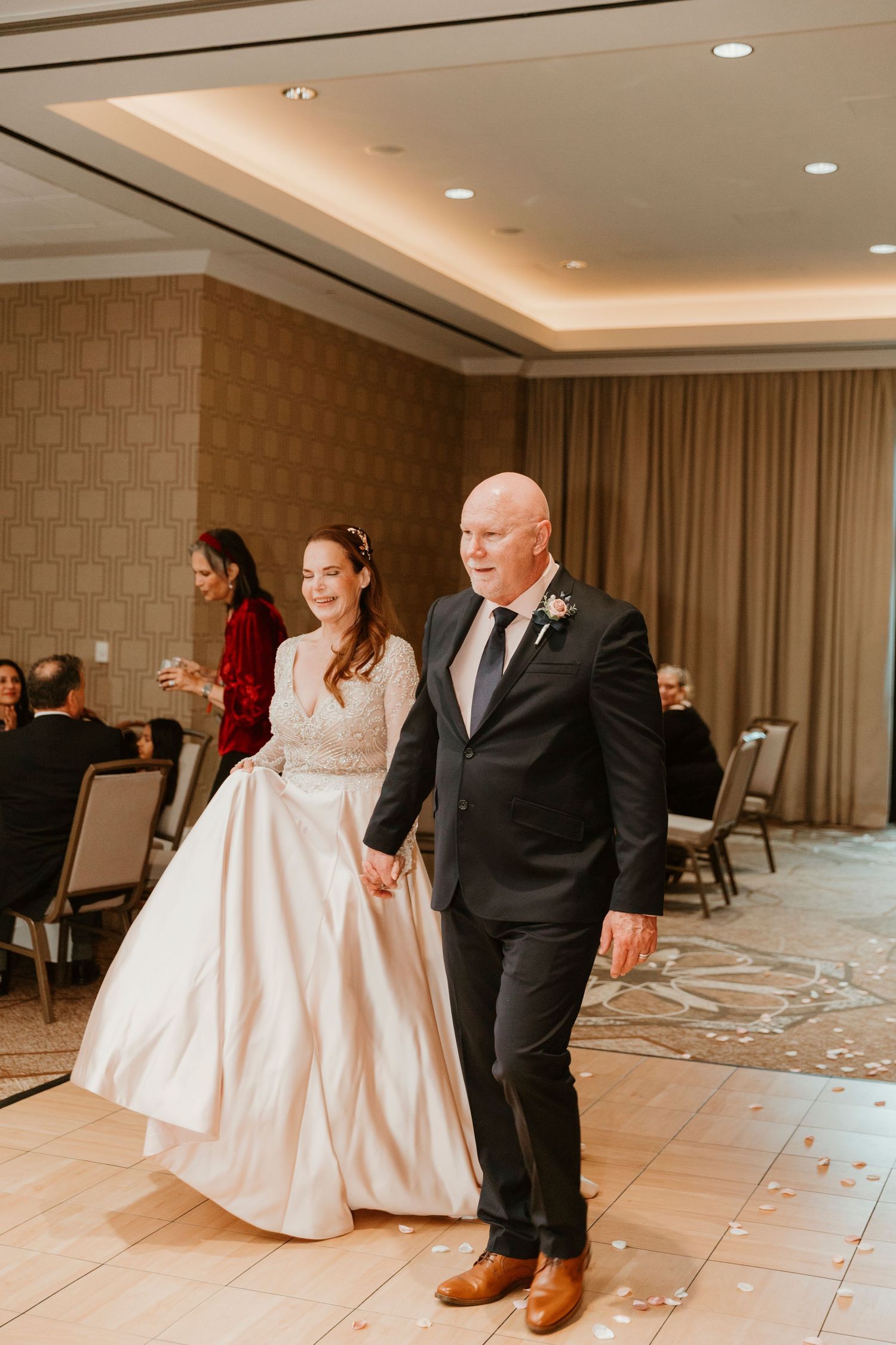 Two wedding guests share a dance together on a tiled floor in an elegant hotel ballroom with warm lighting.
