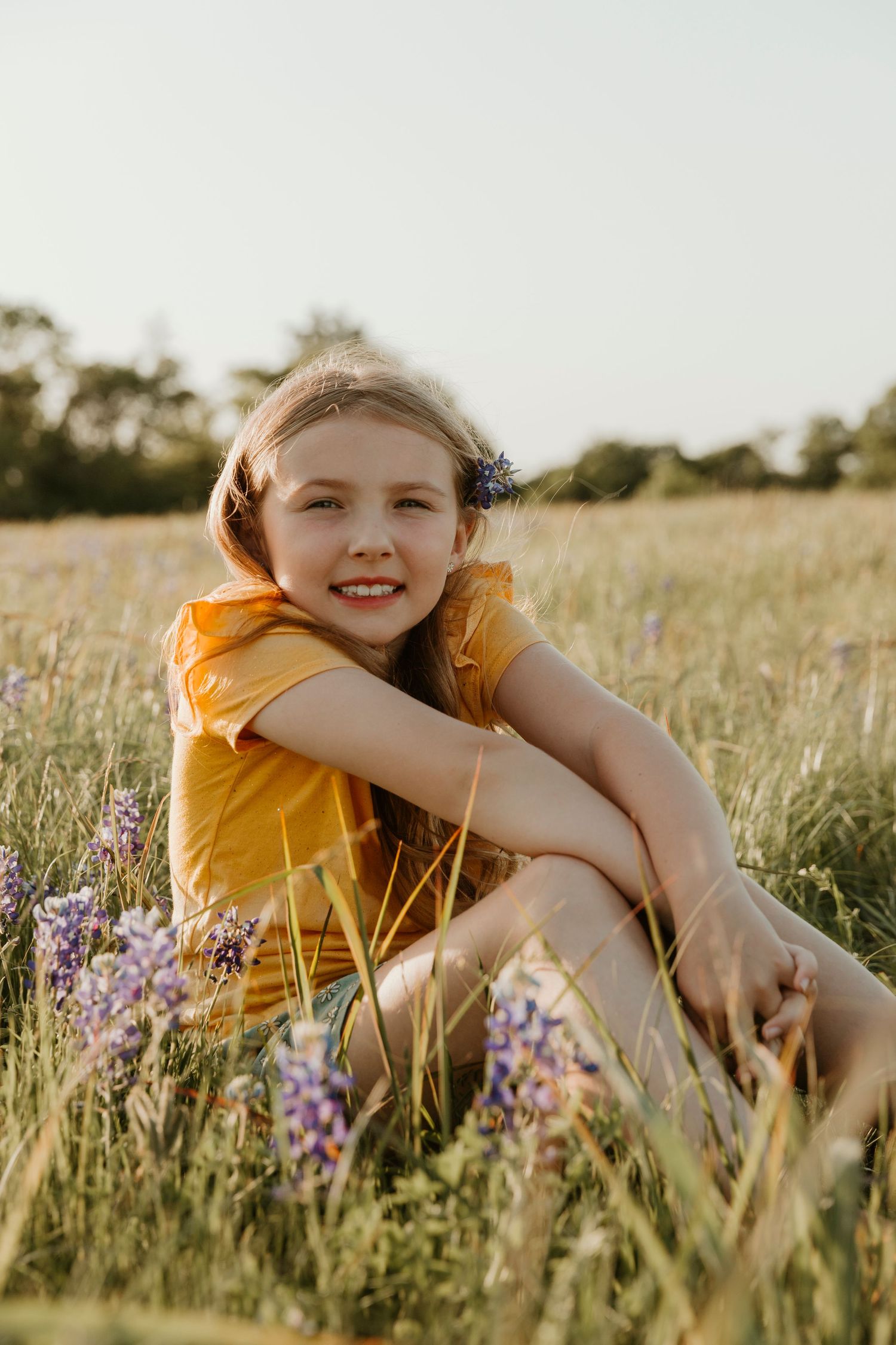 Golden hour portrait in meadow with yellow shirt among purple wildflowers.