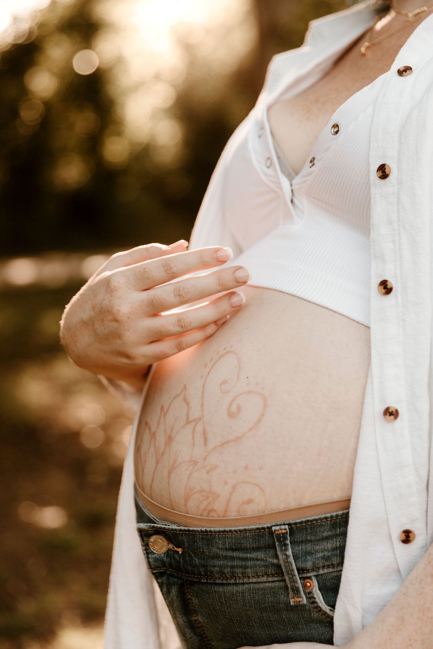A artistic maternity photo showing a decorated belly in warm sunset lighting.