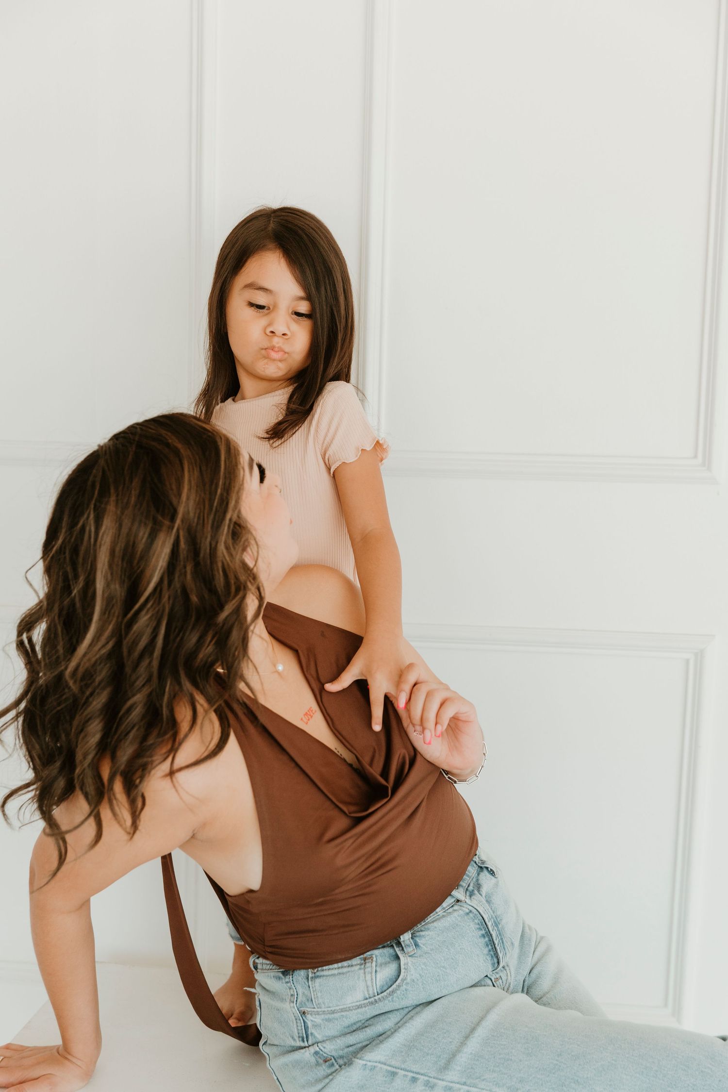 Playful indoor portrait against white wall showing parent-child interaction.