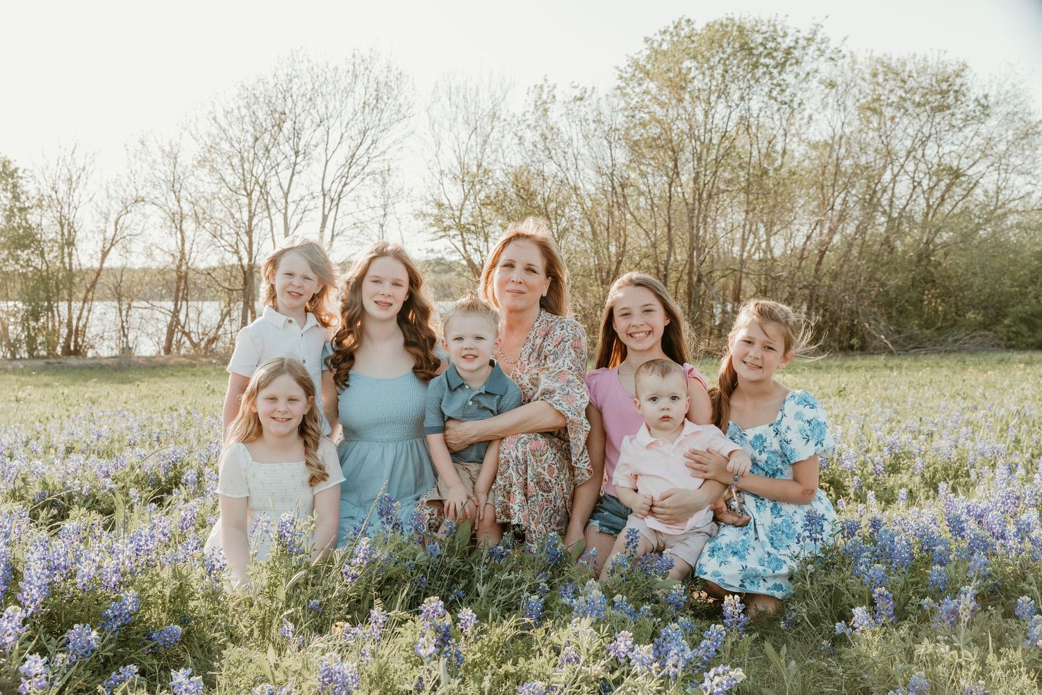 A group sits together in a field of bluebonnets during sunset, wearing coordinating pastel outfits.