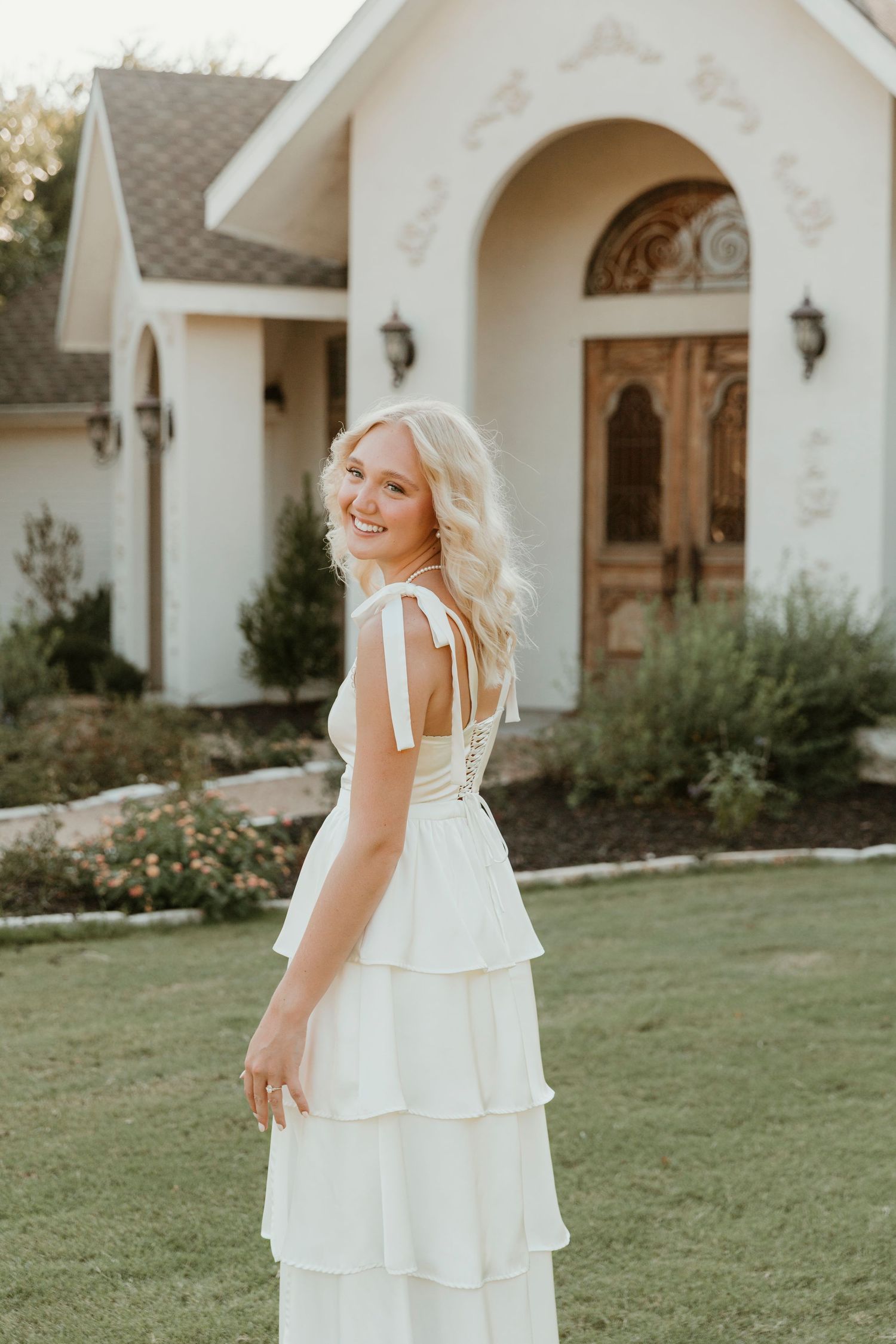 A tiered white dress flows in the garden breeze against a white church backdrop.