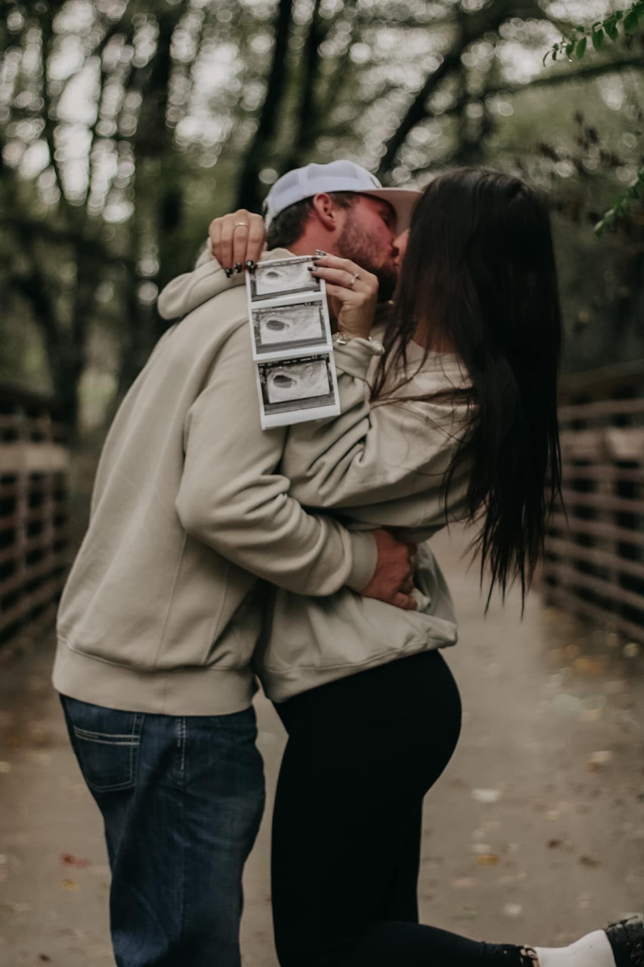 Couple embracing while holding ultrasound photos during pregnancy announcement photoshoot.