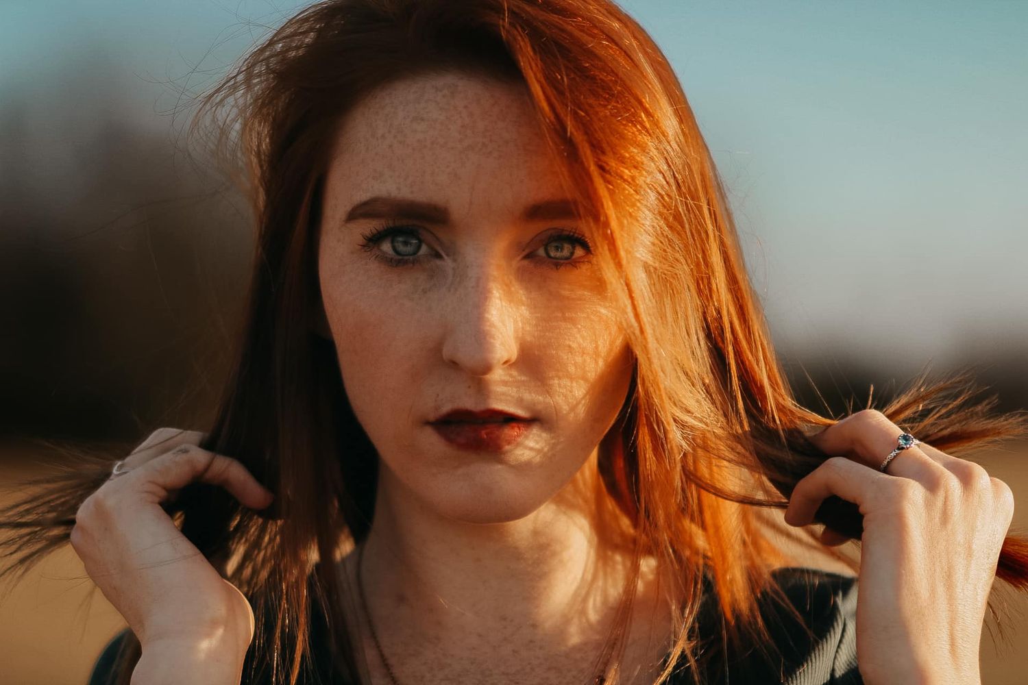 Portrait with warm sunlight illuminating vibrant red hair against a soft blue sky.