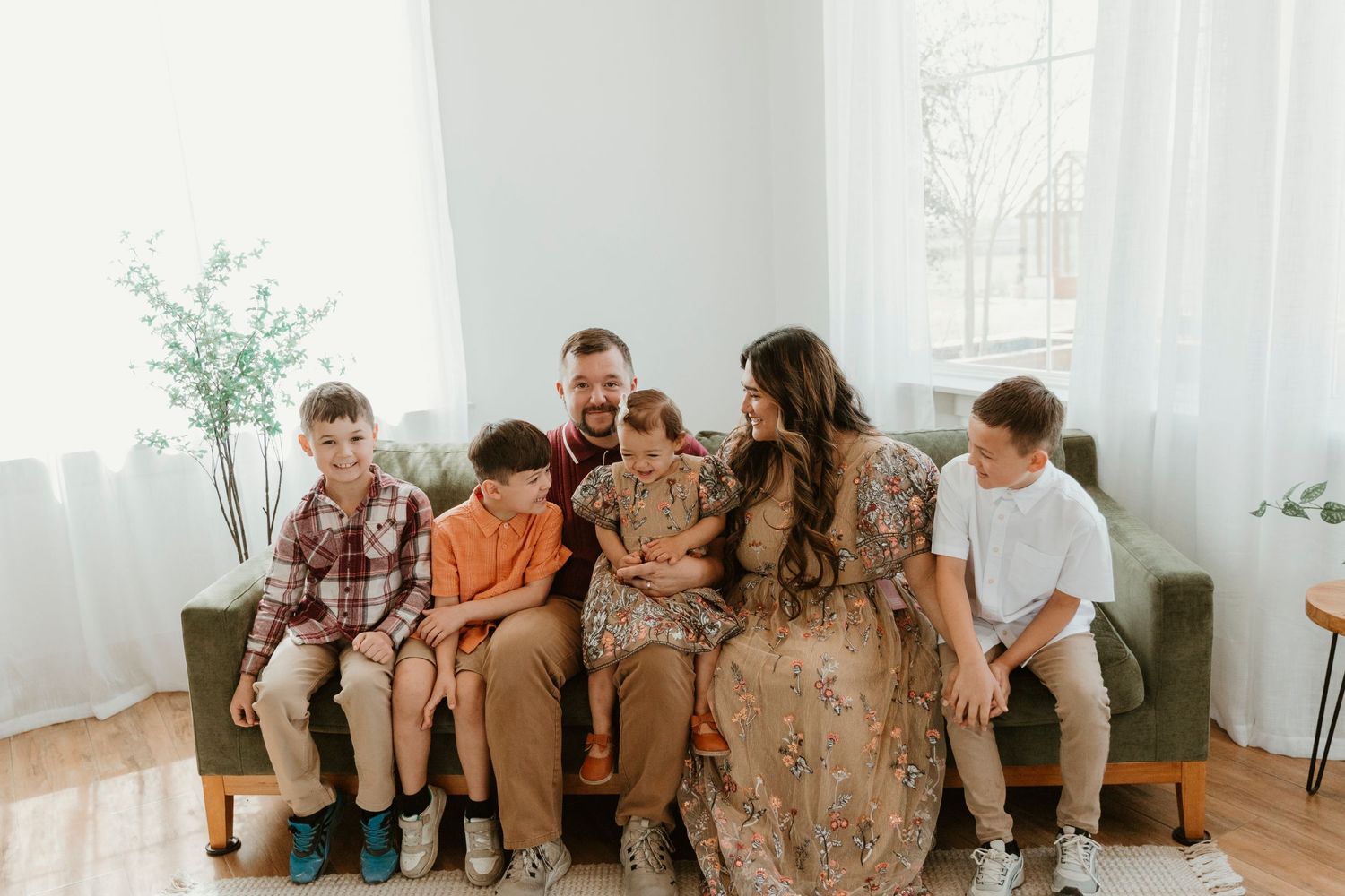 Casual family portrait of group sitting together on green couch in bright white room.