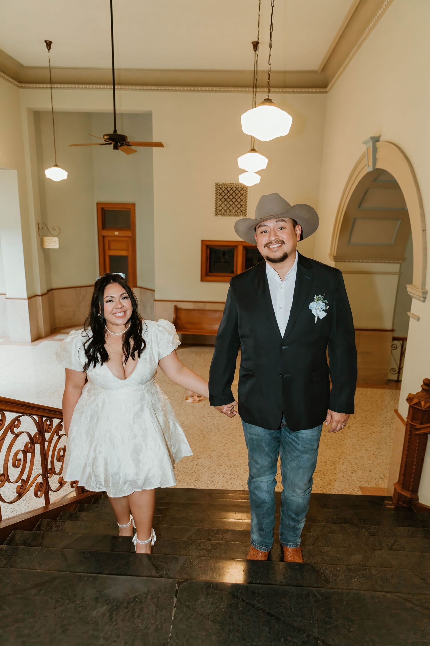 Newlyweds walking down hallway in vintage building with elegant pendant lights.