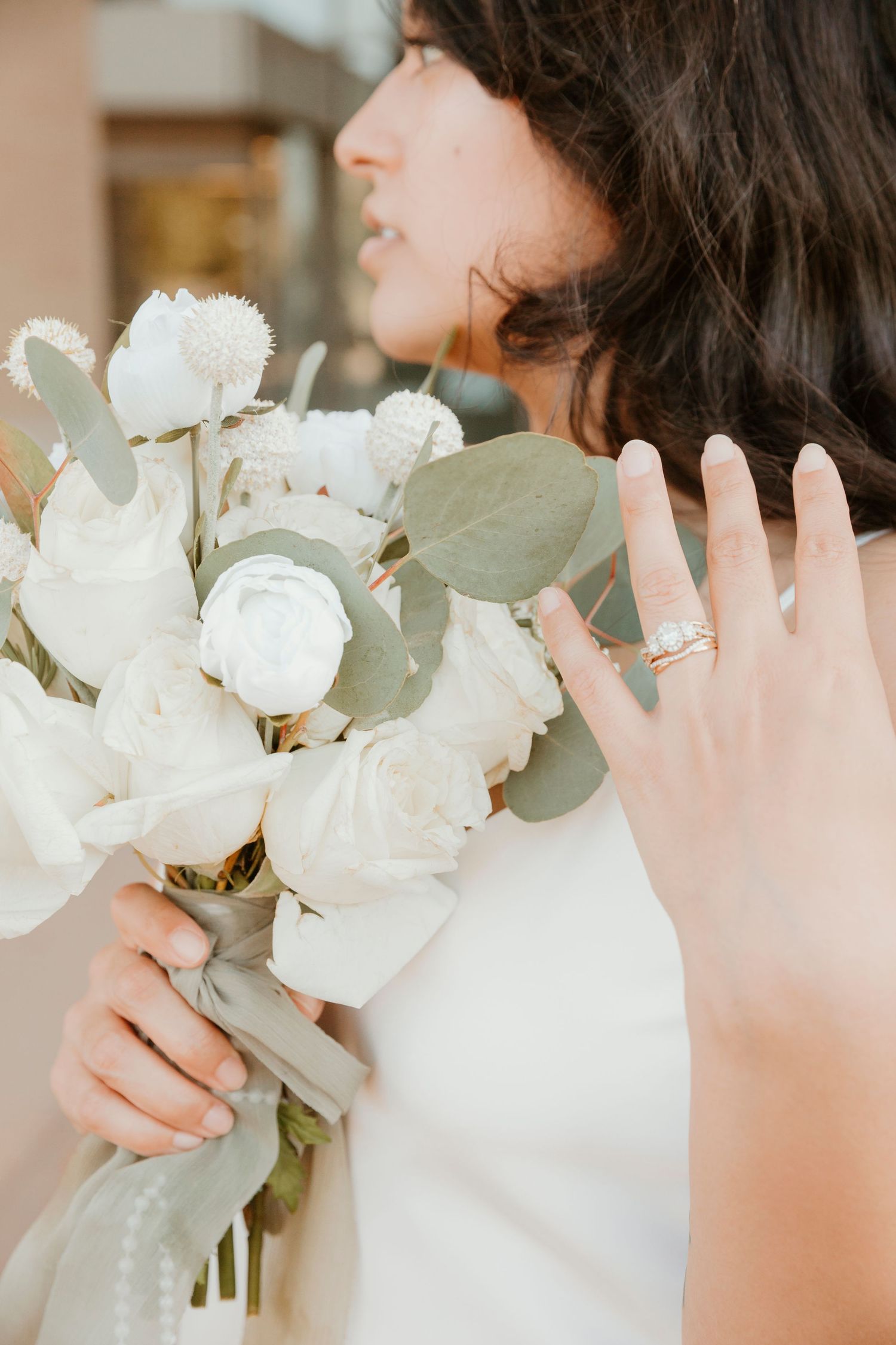 Close-up view of a white peony bouquet with eucalyptus leaves being held against a light background.