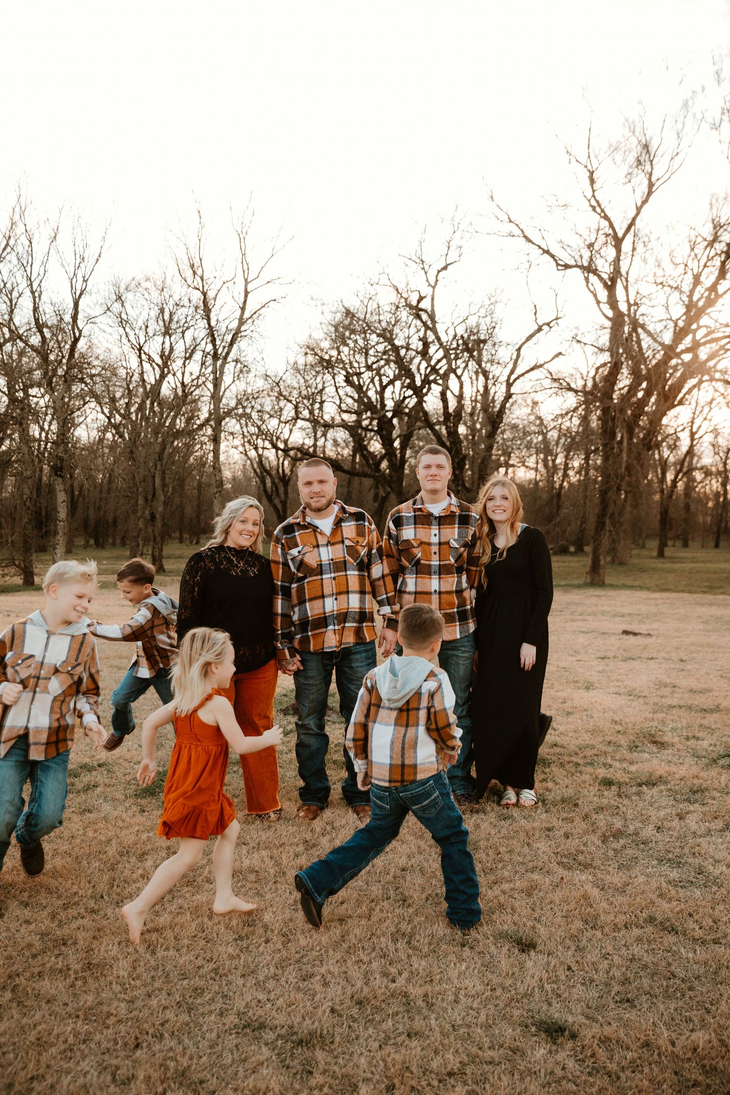 Group in coordinated plaid and dark outfits poses together in a natural outdoor setting at sunset.