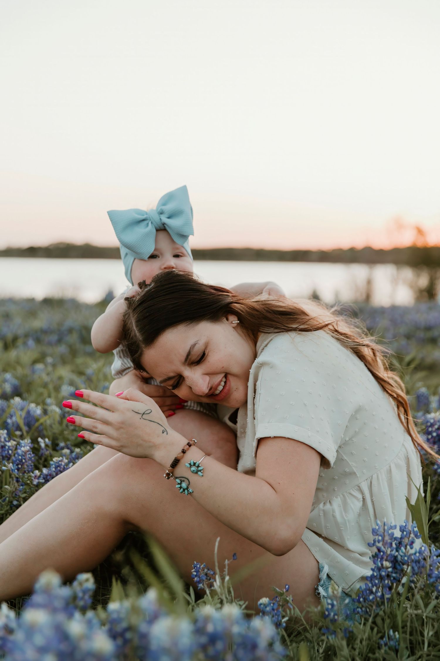 Mother and baby share a sweet moment while sitting in a field of bluebonnets at sunset.