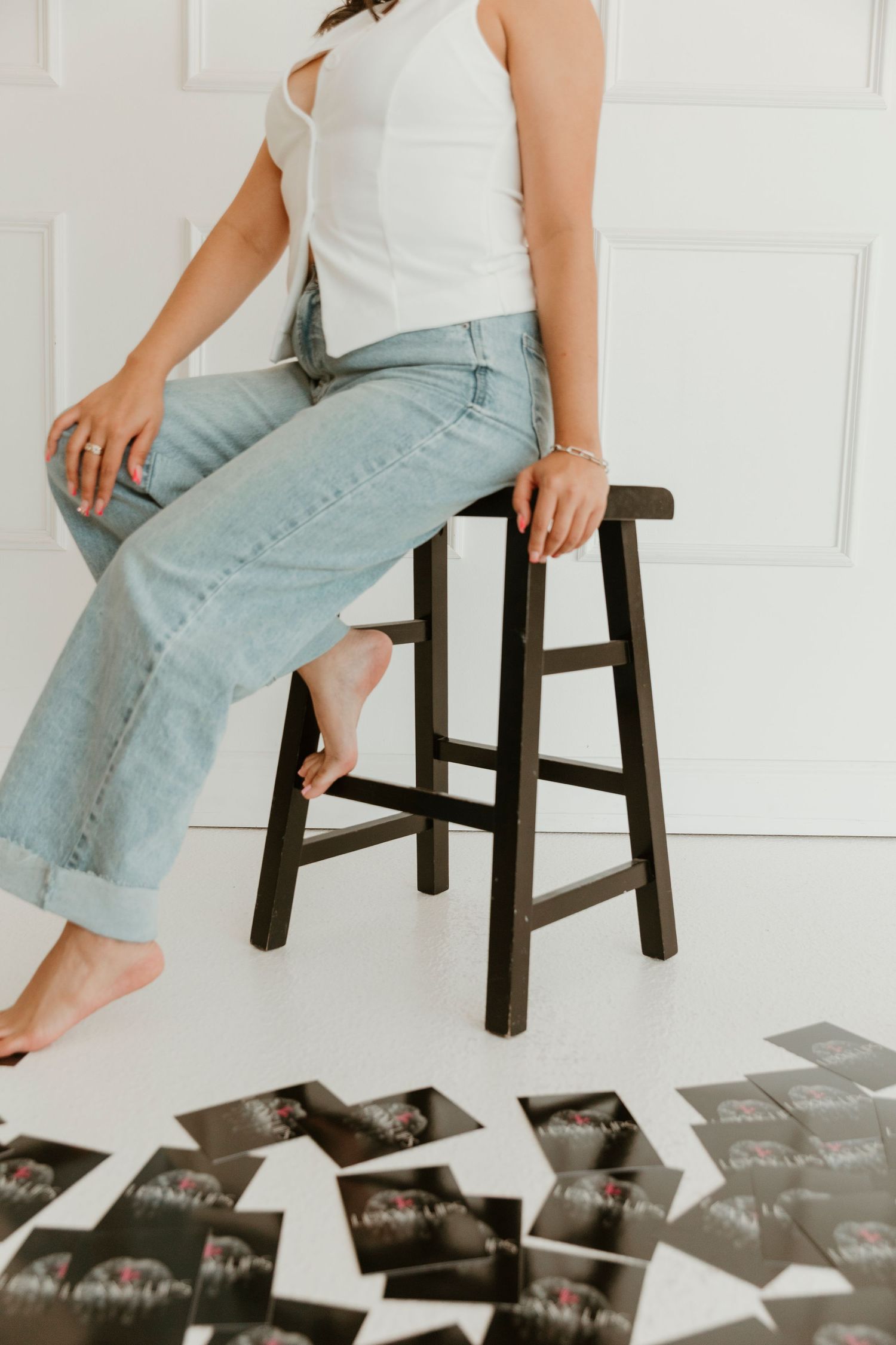 Person sitting on wooden stool wearing white top and light jeans with photos scattered below.