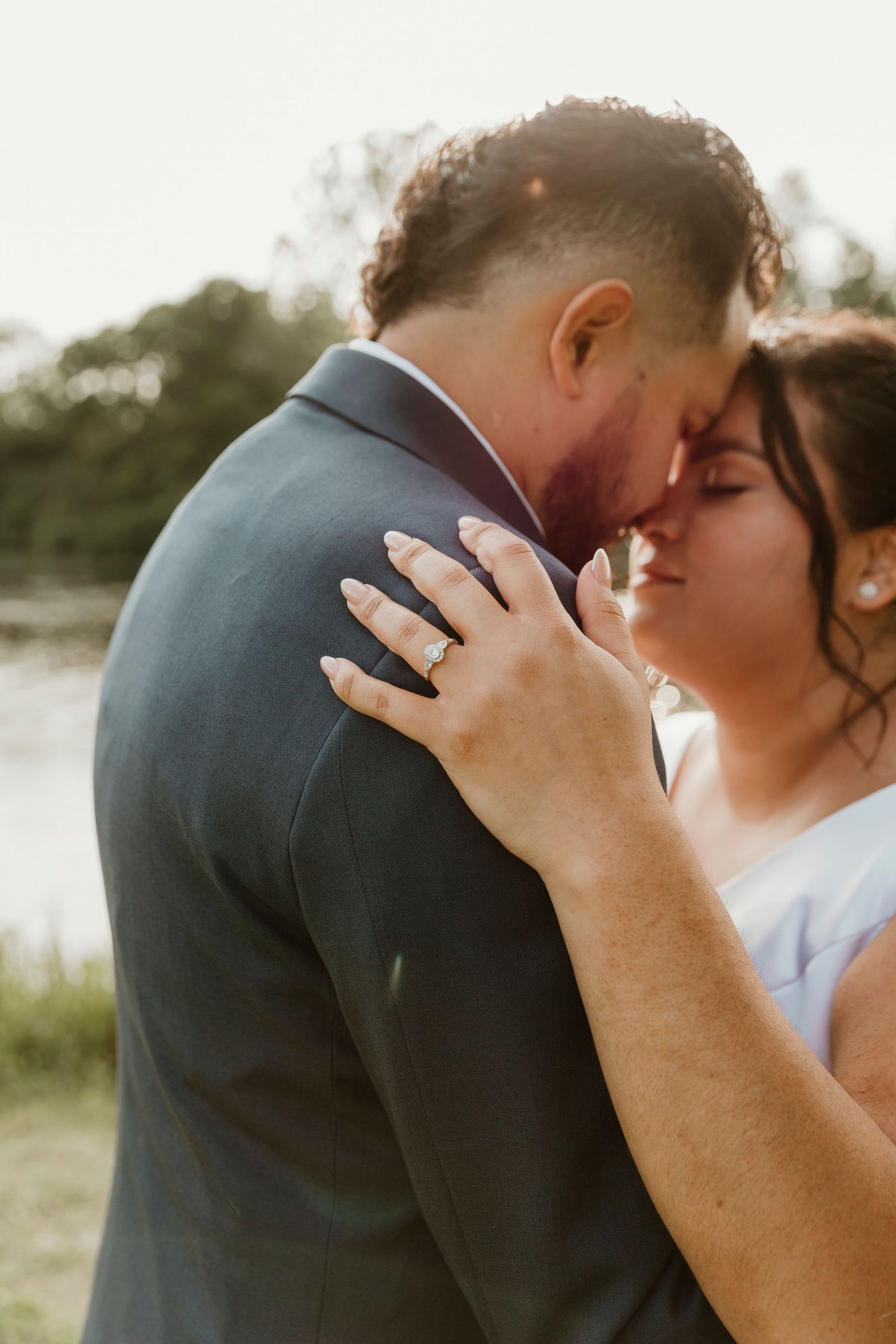 Intimate wedding moment captured at sunset with bride's hand showing engagement ring.