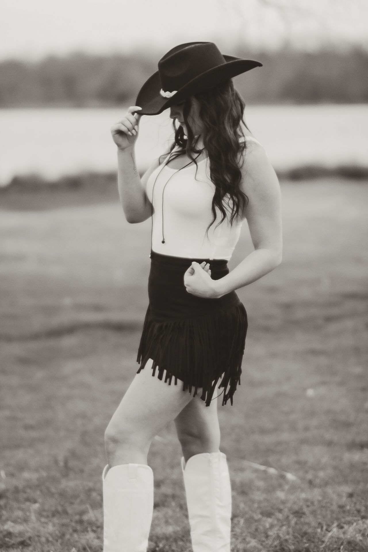 Black and white portrait of woman in western wear with cowboy hat and fringe skirt.
